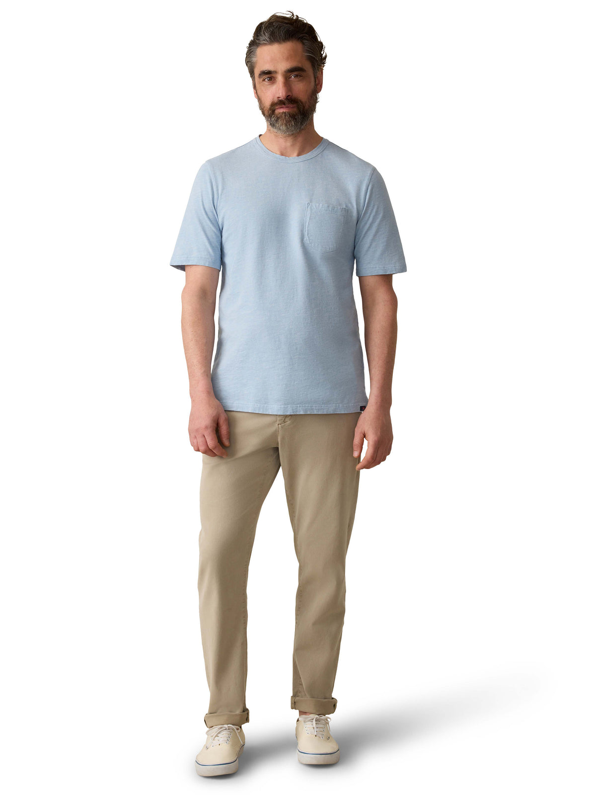 A man wearing a blue tee, beige pants, and sneakers, image 2 of 3