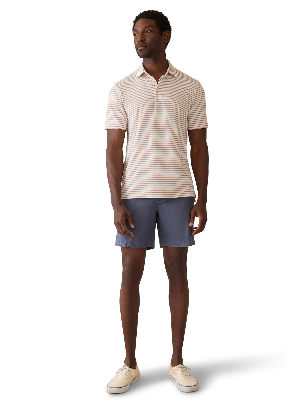 A man wearing a striped polo shirt, blue shorts, and sneakers, image 2 of 3