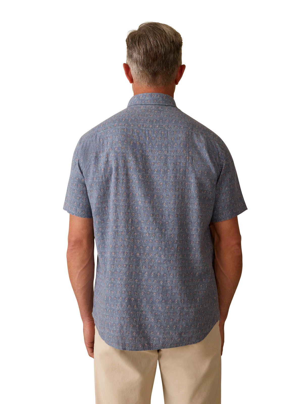 A man viewed from behind wearing a blue printed button down shirt and beige shorts, image 3 of 3