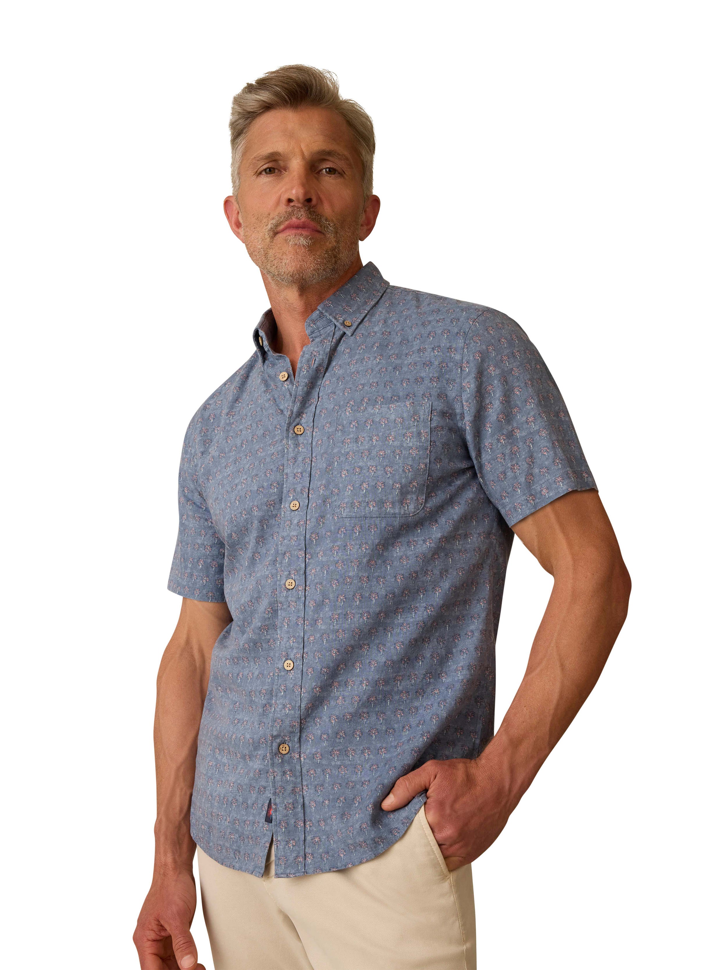A man wearing a blue printed button down shirt and beige pants
