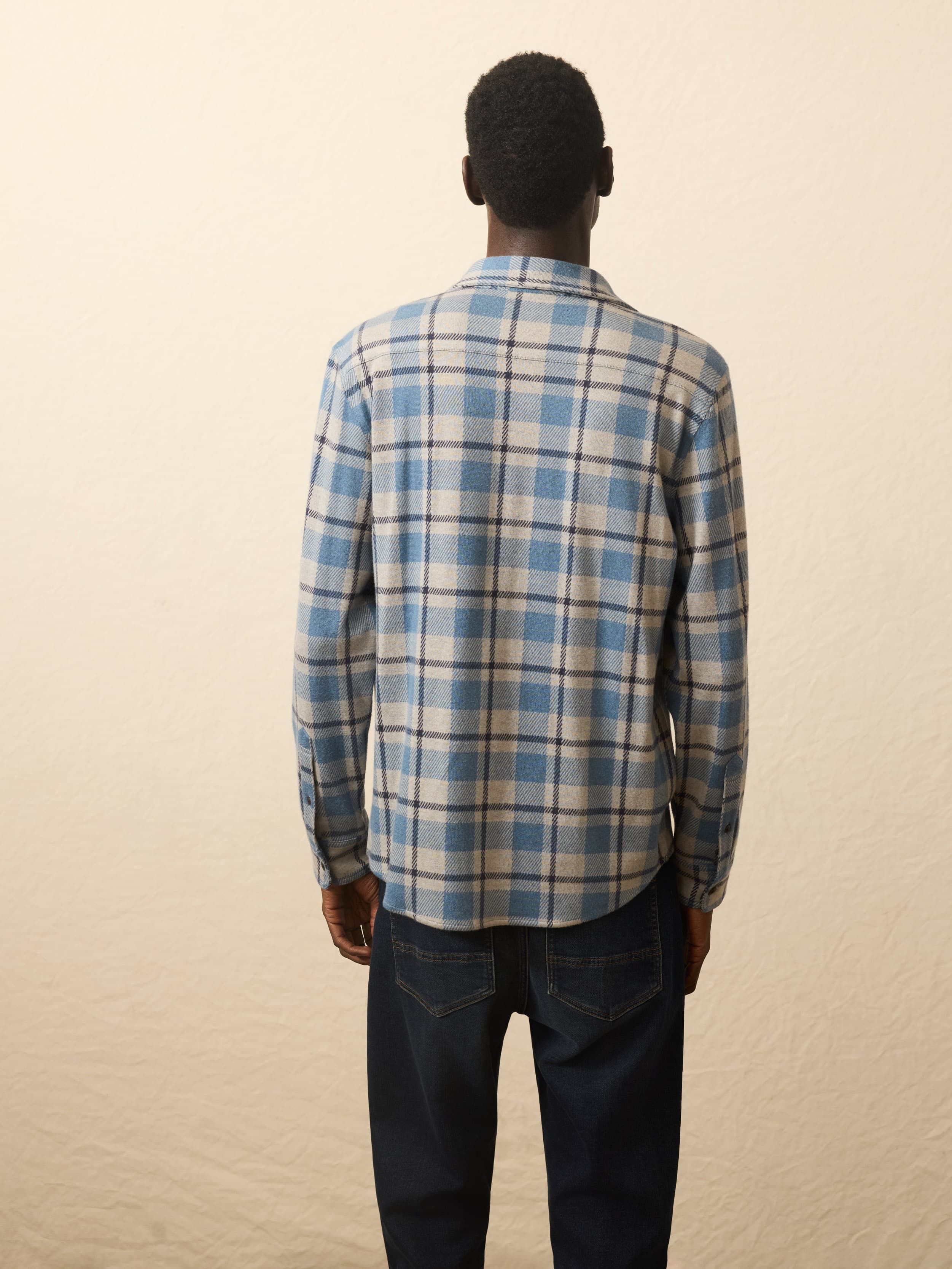 Back view of a man wearing a blue and beige plaid shirt against a beige background