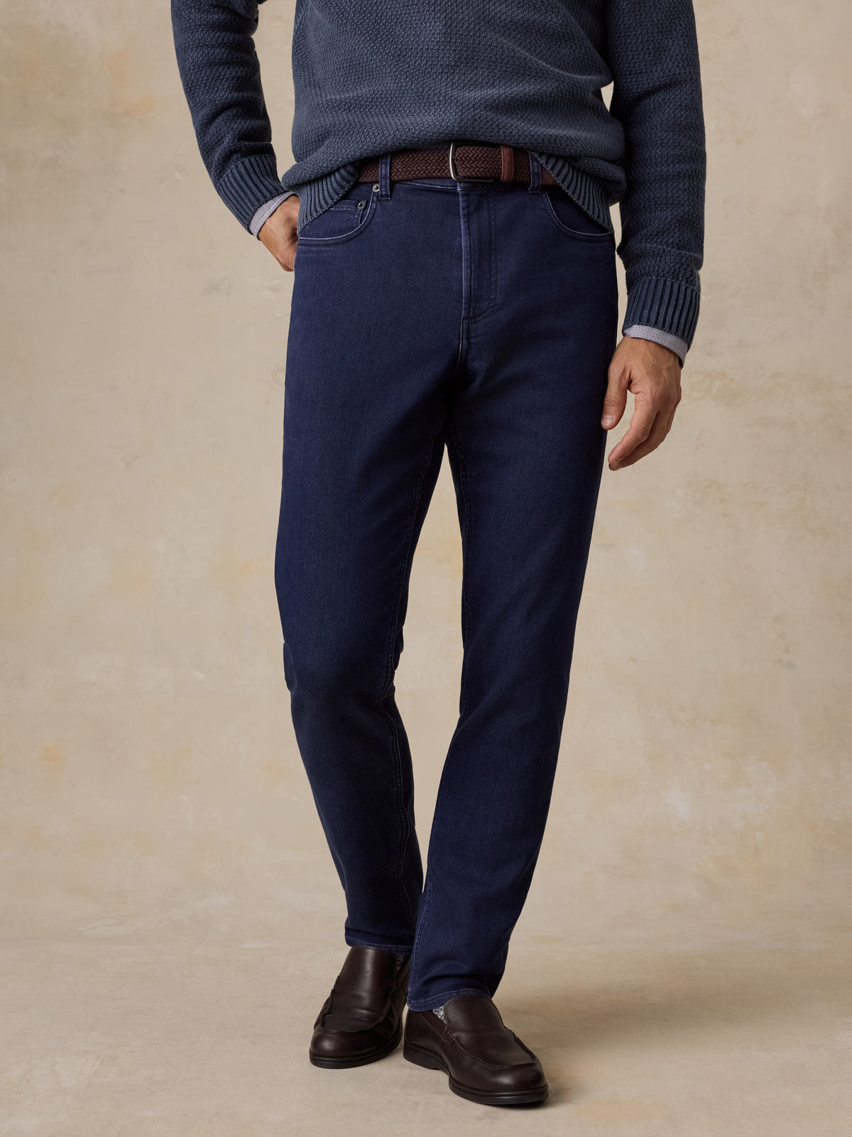A man wearing a blue sweater, blue jeans, and black shoes, image 1 of 5