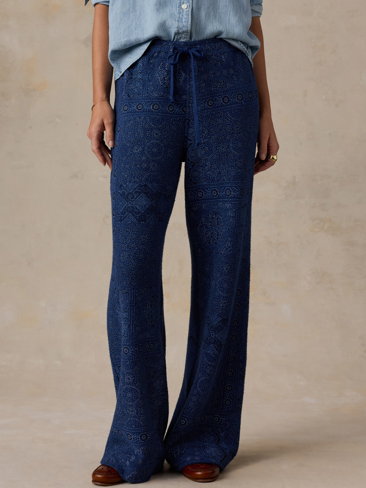 Woman wearing a printed pair of blue pants standing against a beige studio background, image 2 of 7