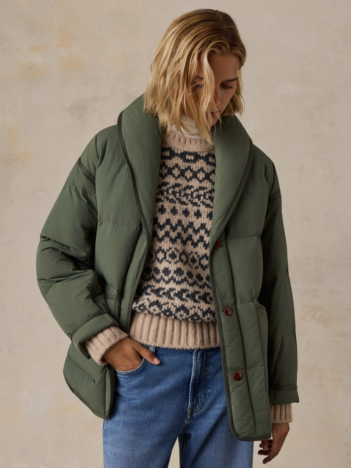 A woman wearing a green jacket over a knit sweater and blue jeans, image 5 of 8