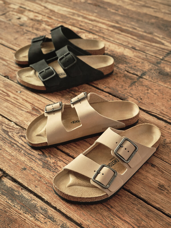 A lifestyle short of Birkenstock + Faherty collection on a rustic wooden floor