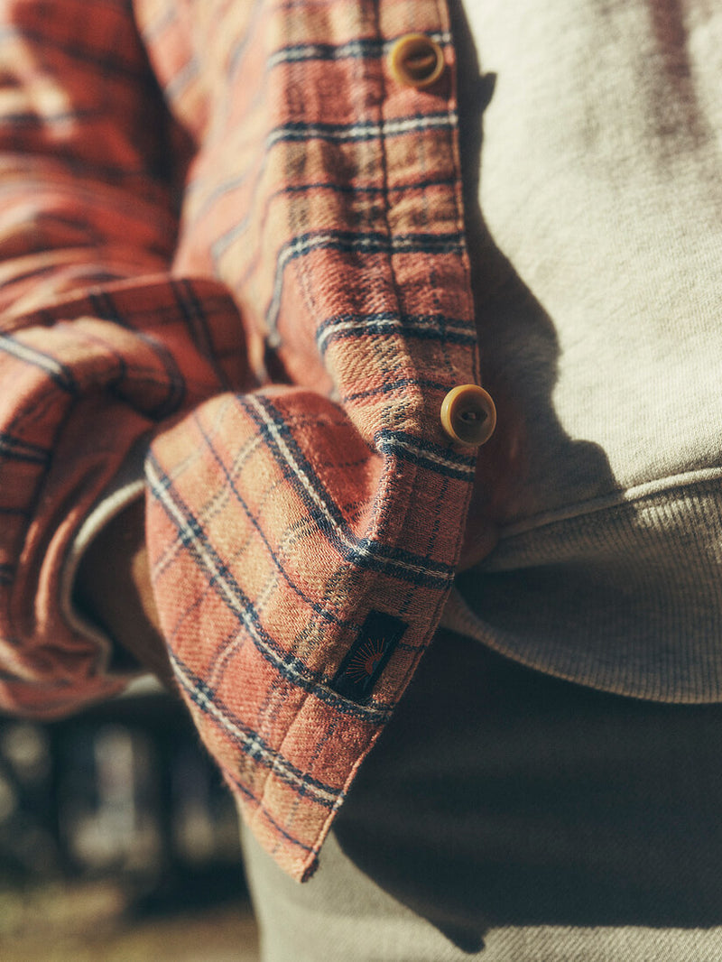 close up of model wearing Belmar work shirt, detailing brown buttons, blue and pink plaid and signature faherty patch