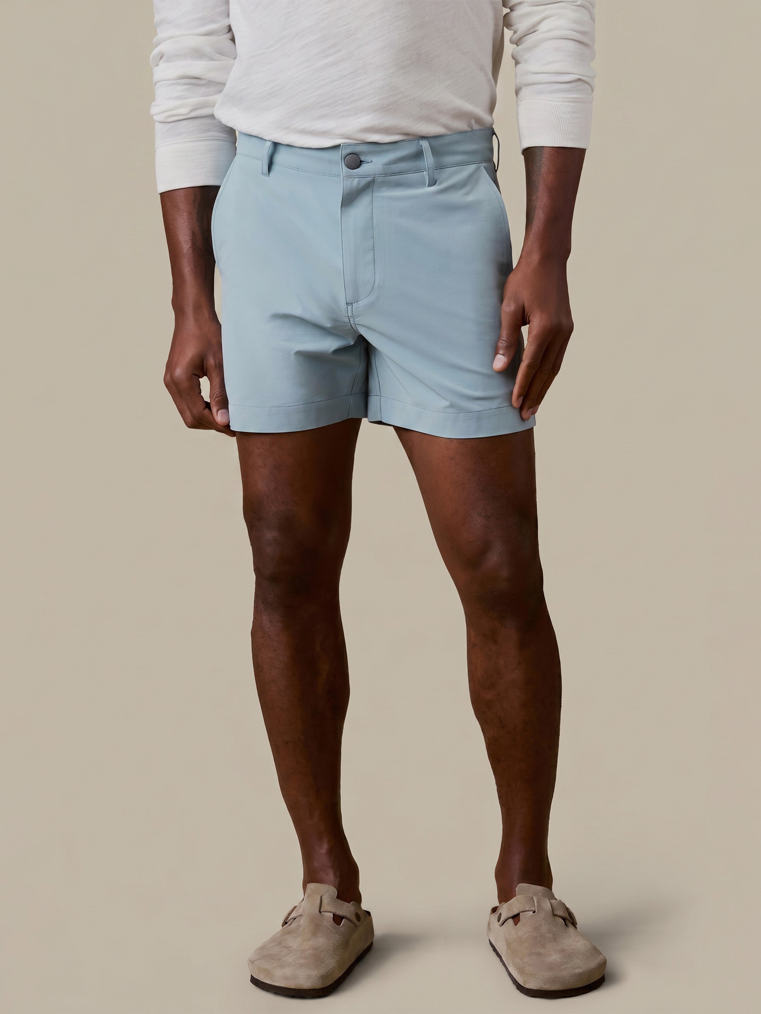 Man wearing light blue shorts and a white long-sleeve shirt on a beige background