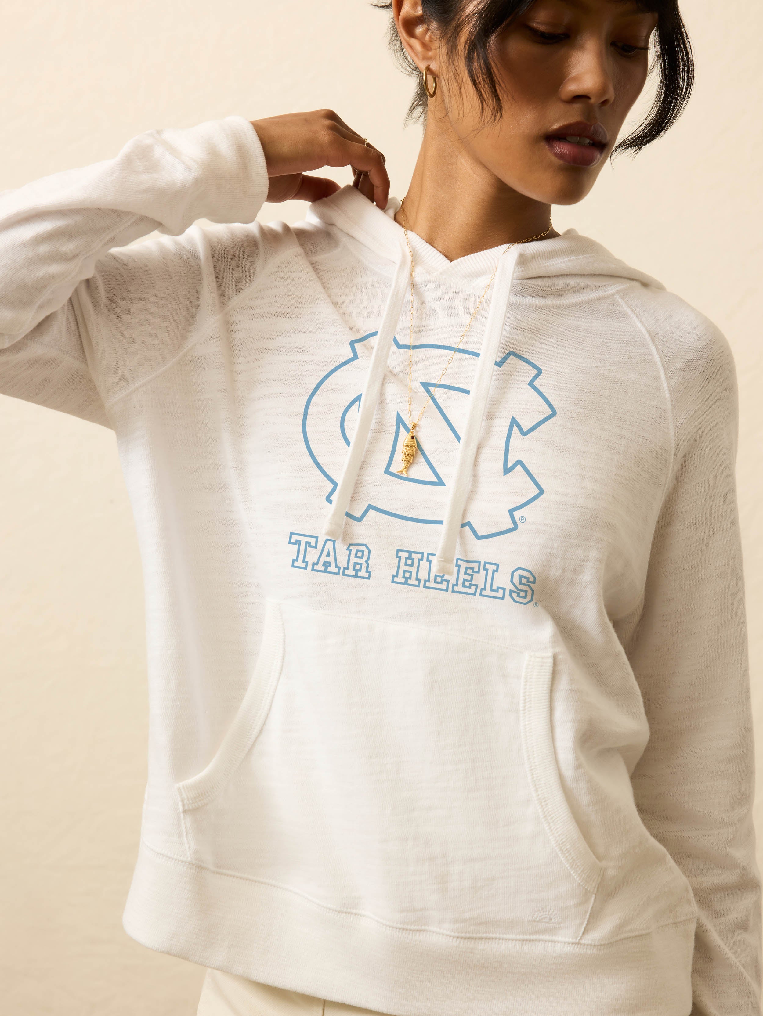 Woman is wearing a white hoodie with UNC graphic at the center front against a beige background