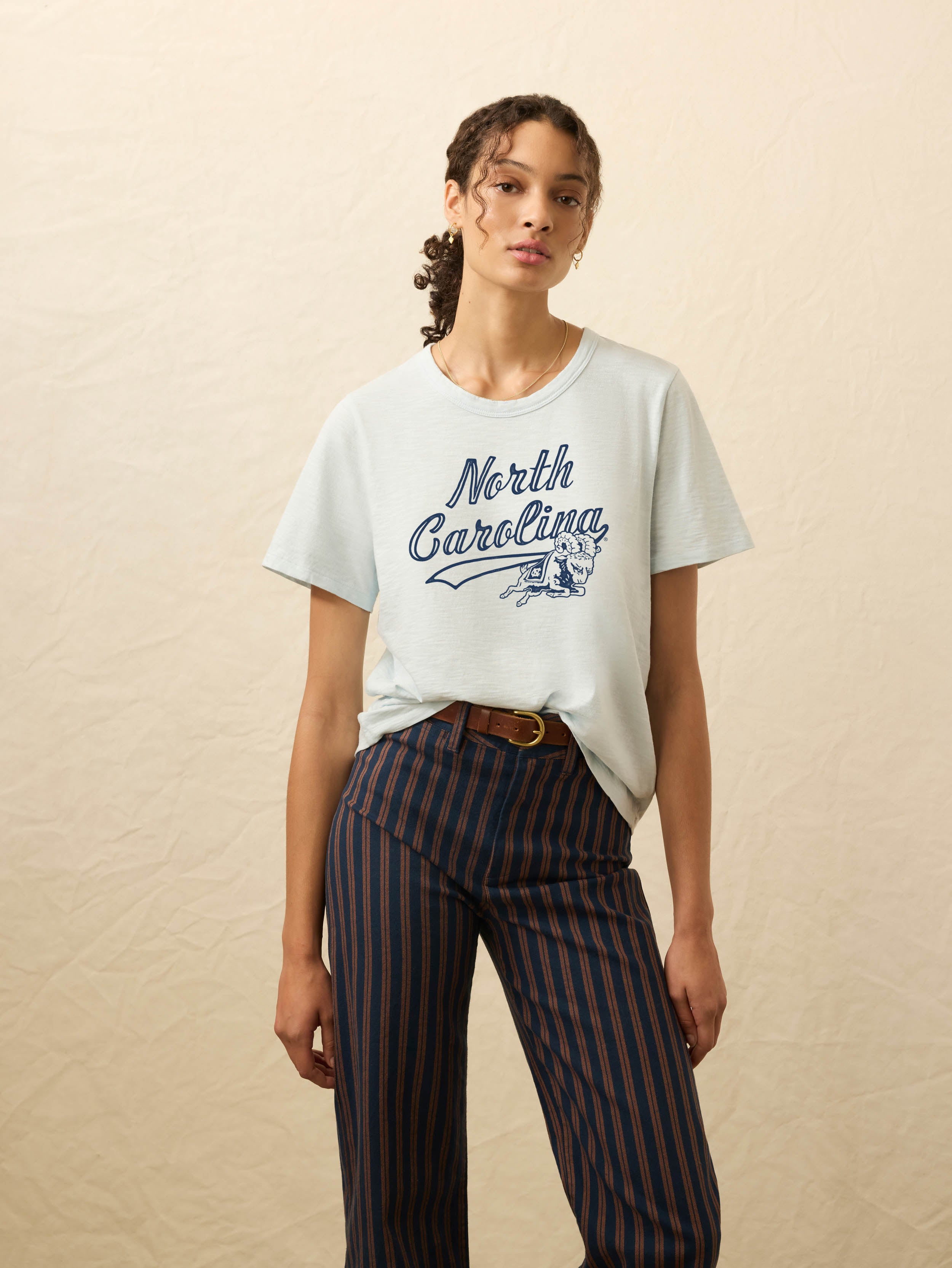 Woman wearing a light blue short sleeve t-shirt with UNC graphic on the center chest against a beige background