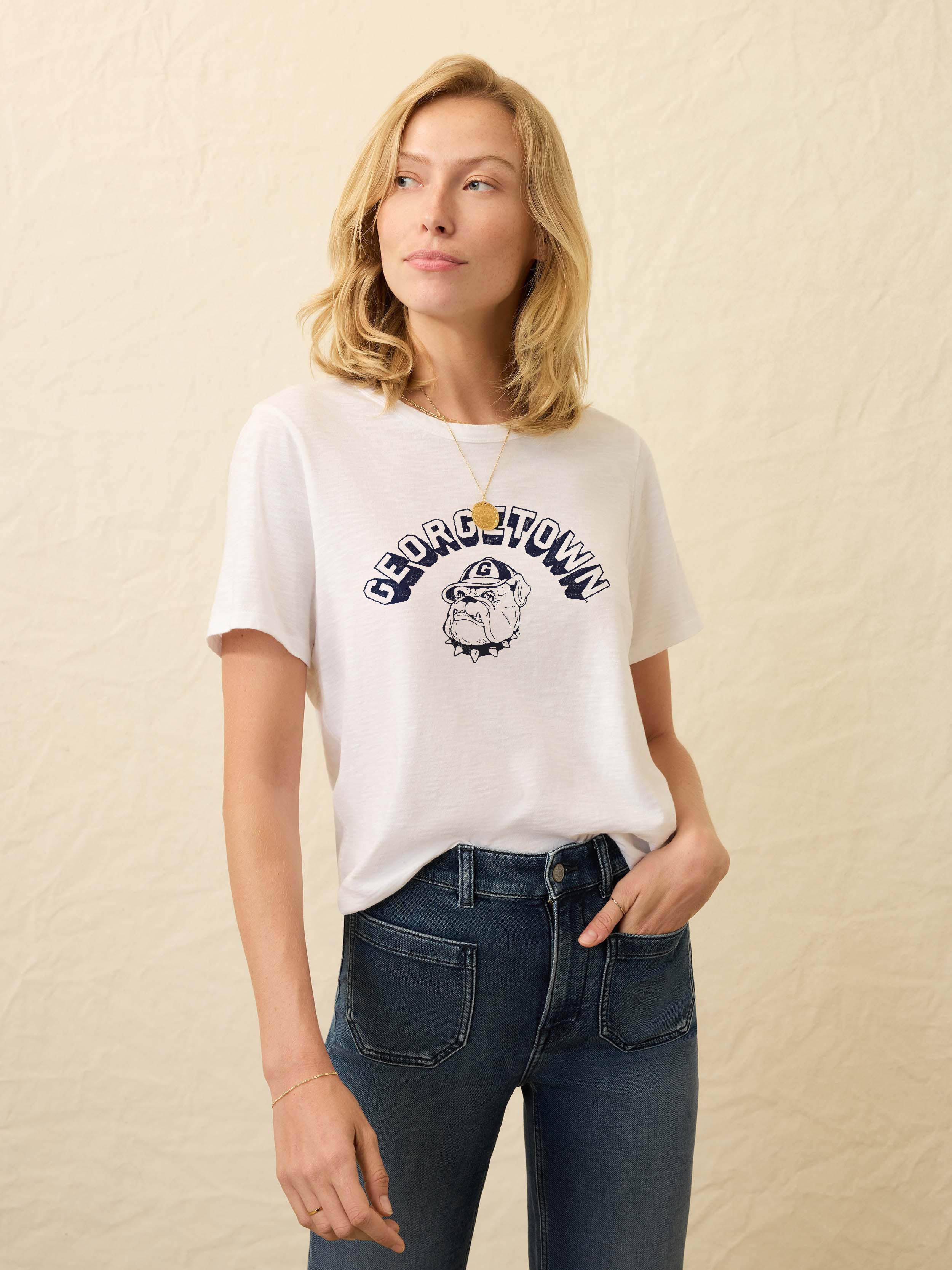 Woman wearing a white t-shirt with Georgetown graphic on the front against a beige background