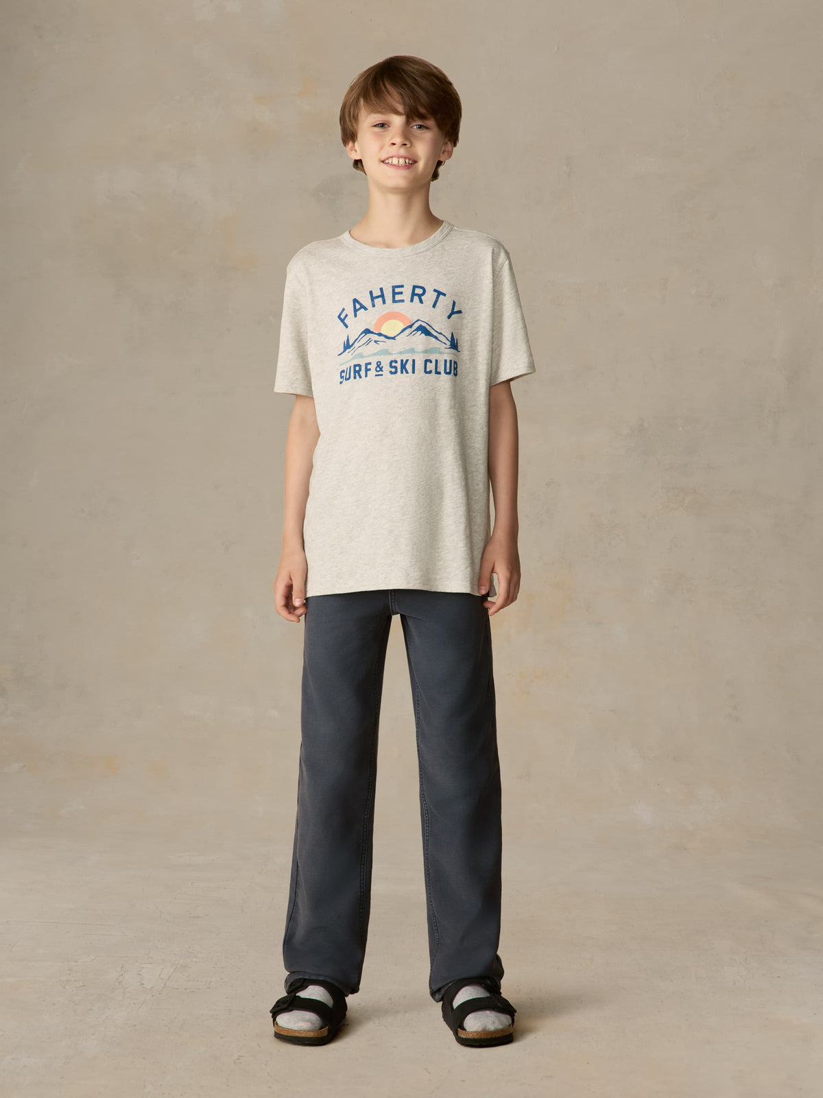 Child wearing a grey surf & ski club tee and black pants against a beige background, image 1 of 4