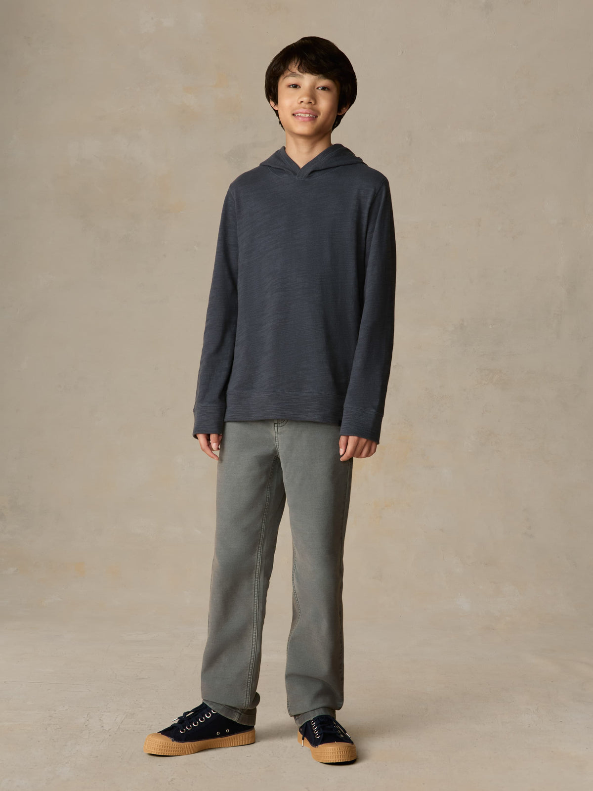 Child wearing a navy hoodie and grey pants against a beige background, image 1 of 5