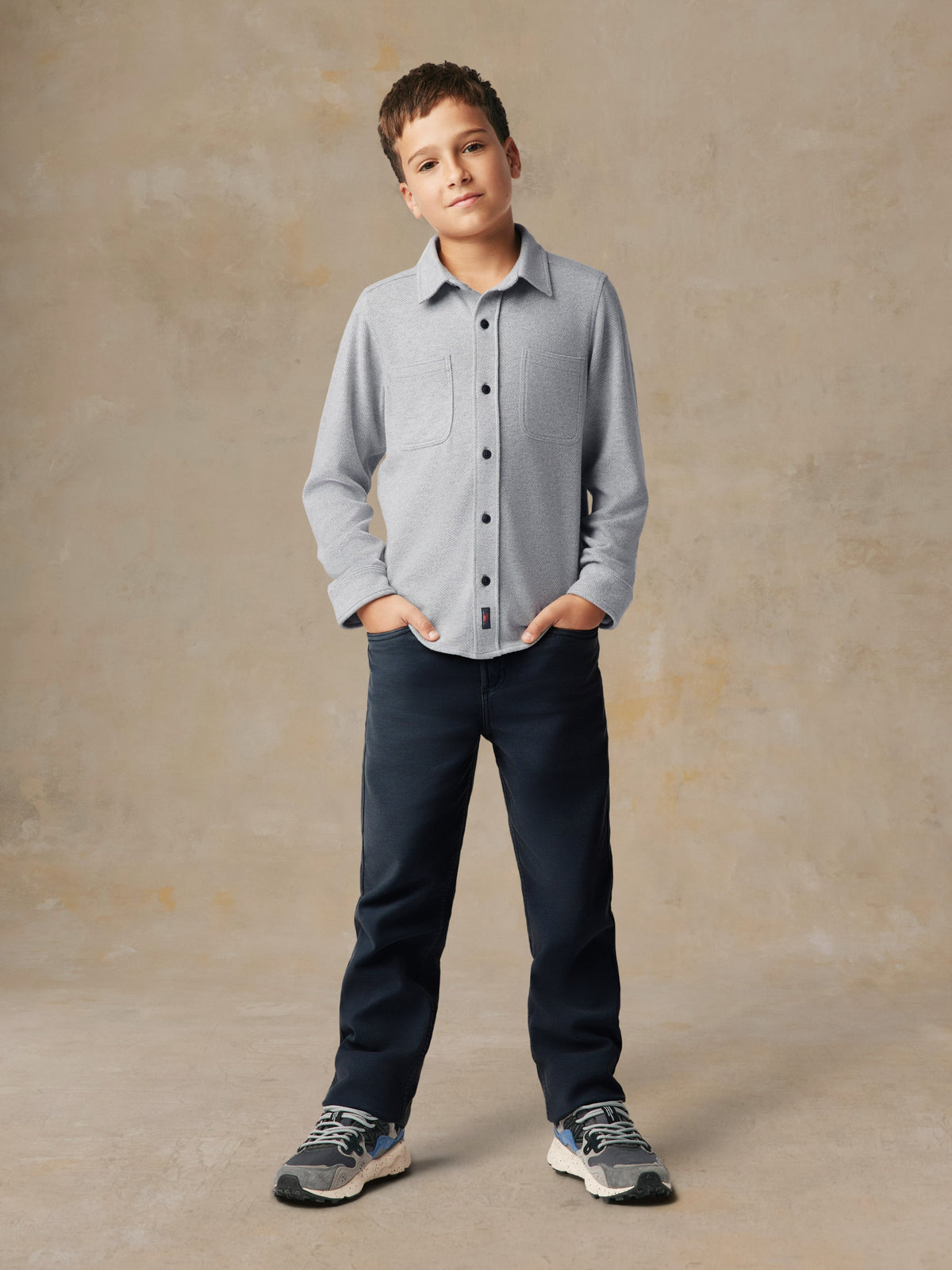 A child wearing a grey button up shirt and black pants, image 1 of 7