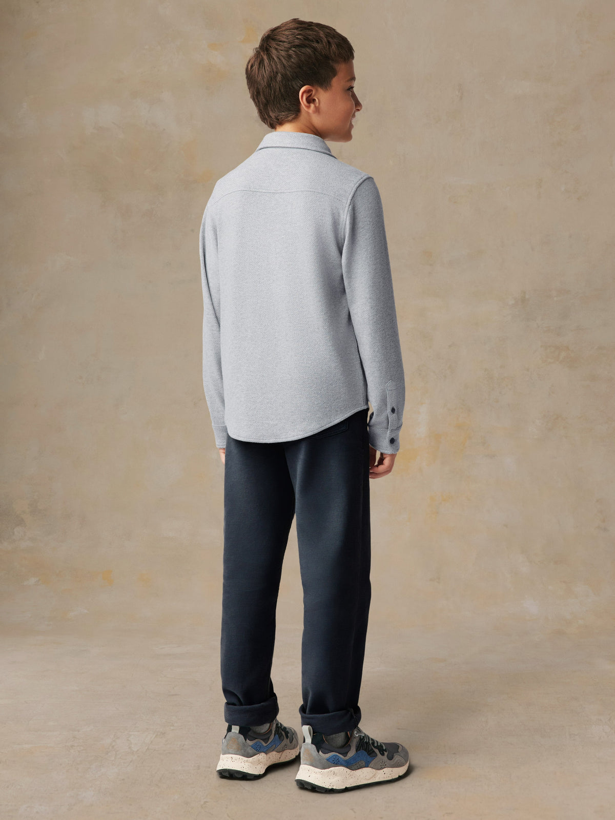 A child viewed from behind wearing a grey button up shirt and black pants, image 3 of 7