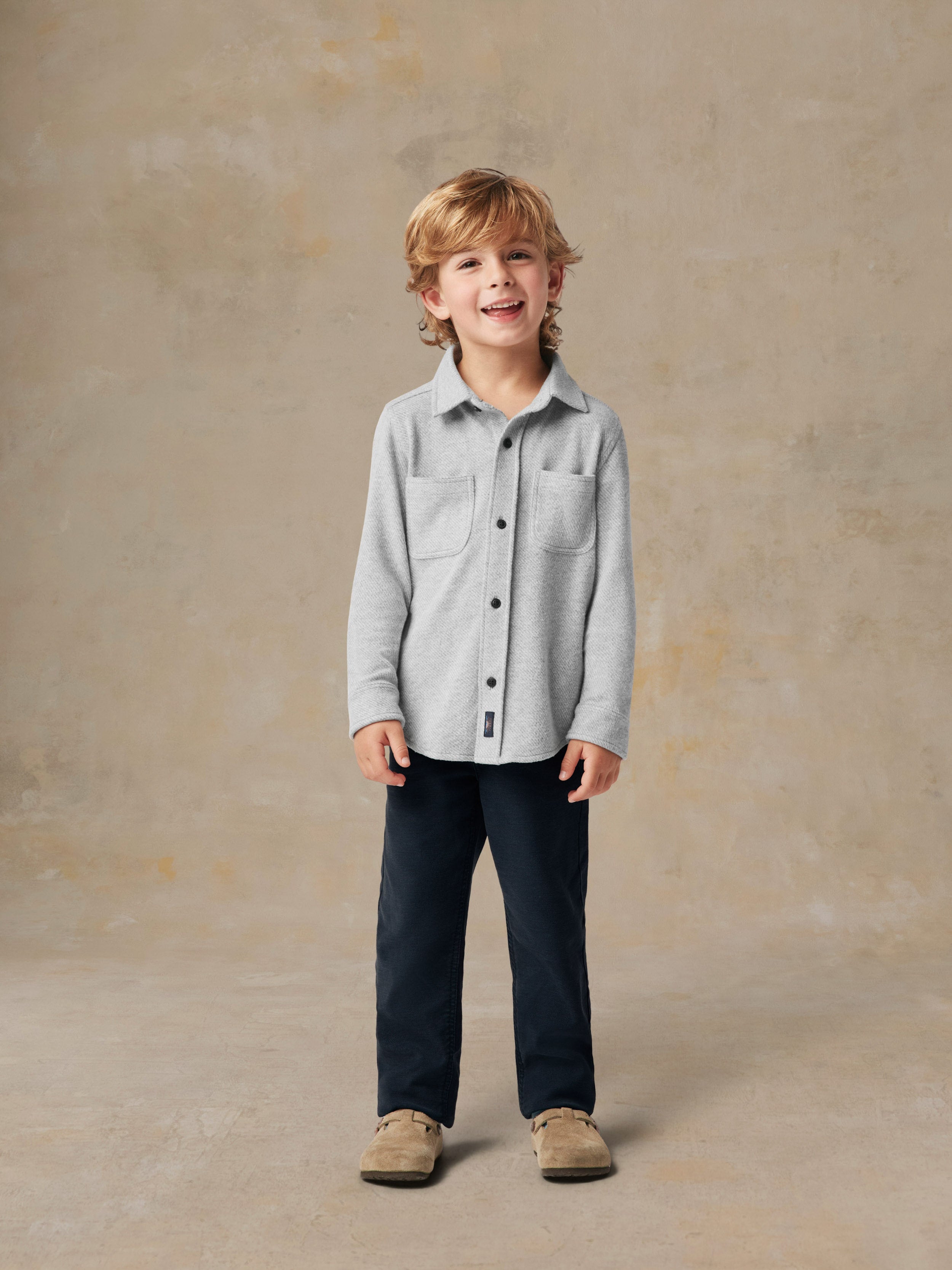 A child wearing a grey button up shirt and black pants