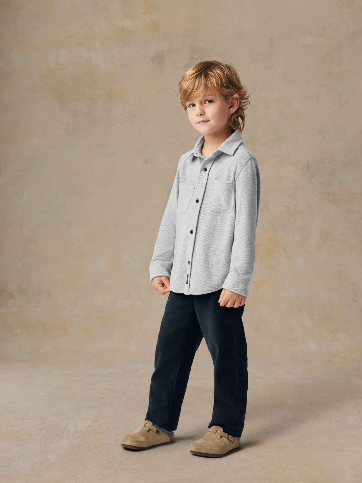 A child wearing a grey button up shirt and black pants, image 3 of 6