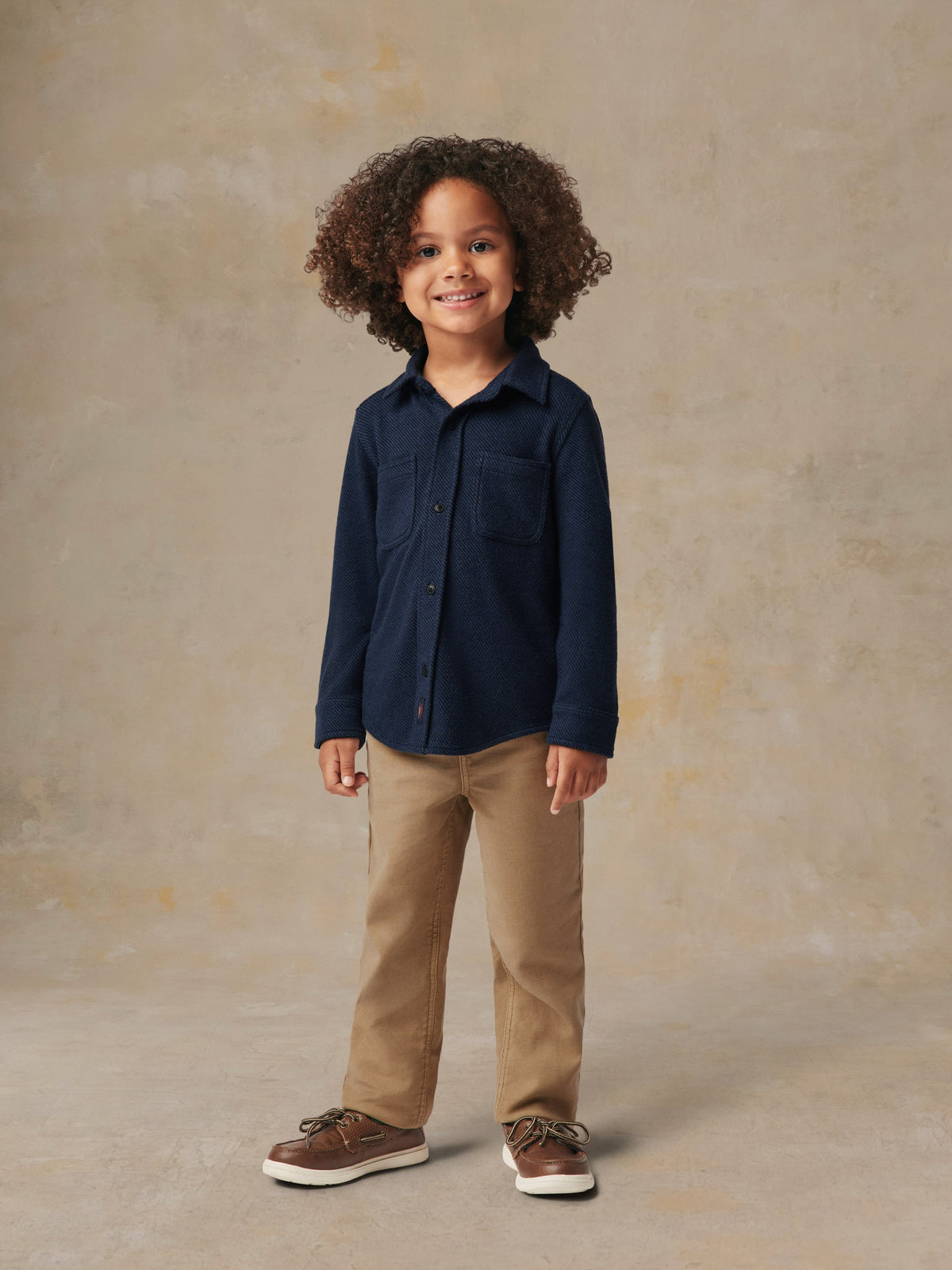 A child wearing a blue button up shirt and beige pants, image 1 of 6