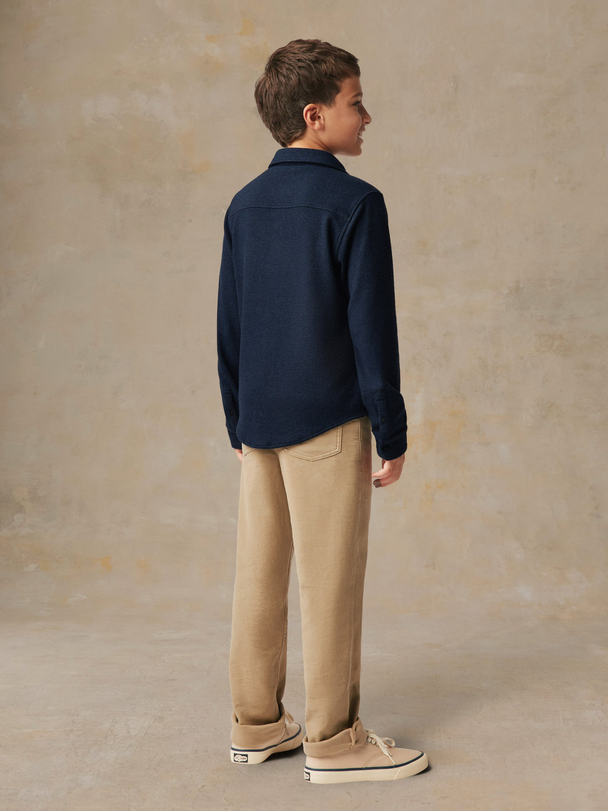 A child viewed from behind wearing a blue button up shirt and beige pants, image 5 of 6