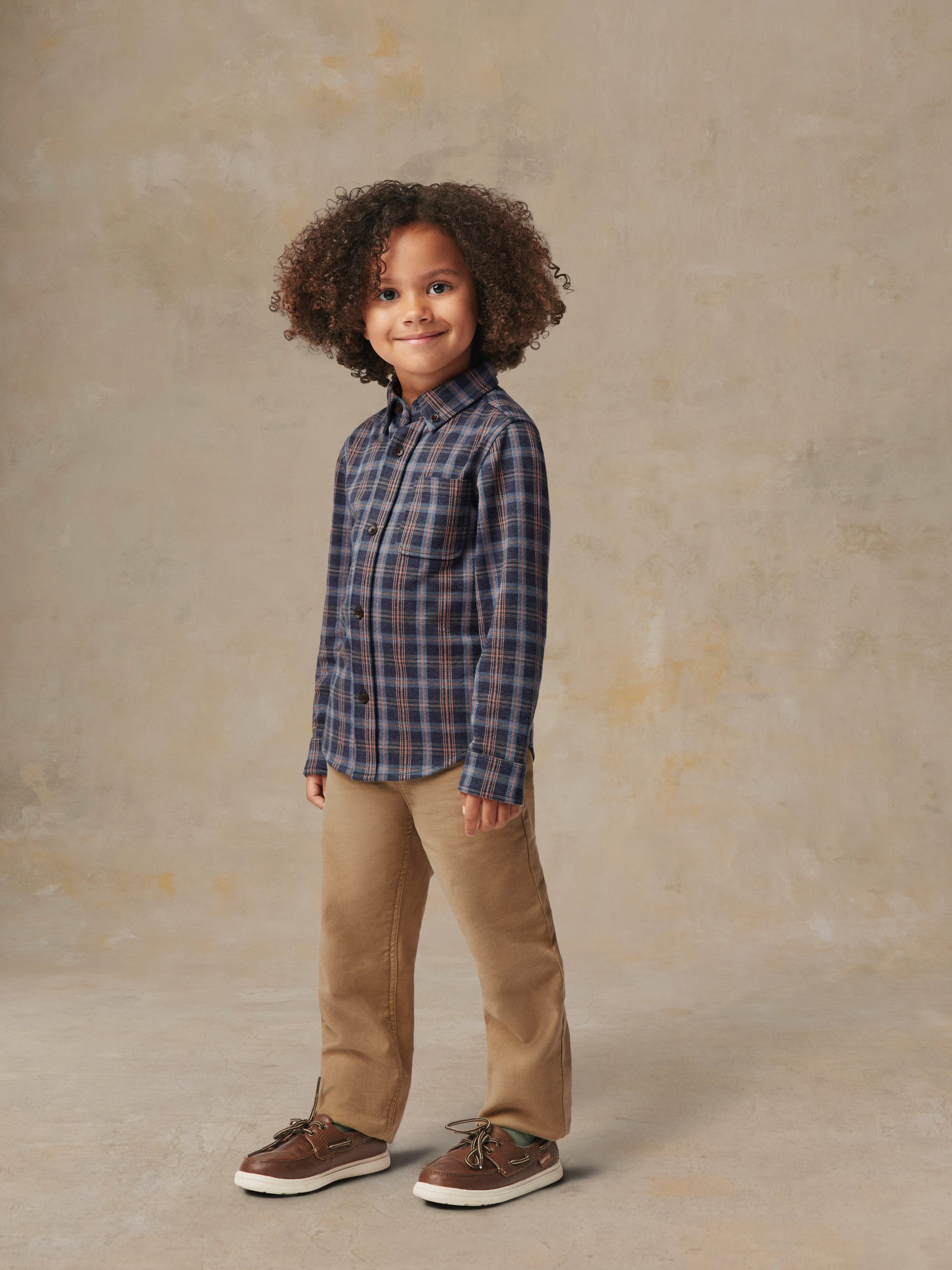 A child is wearing a plaid shirt and beige pants