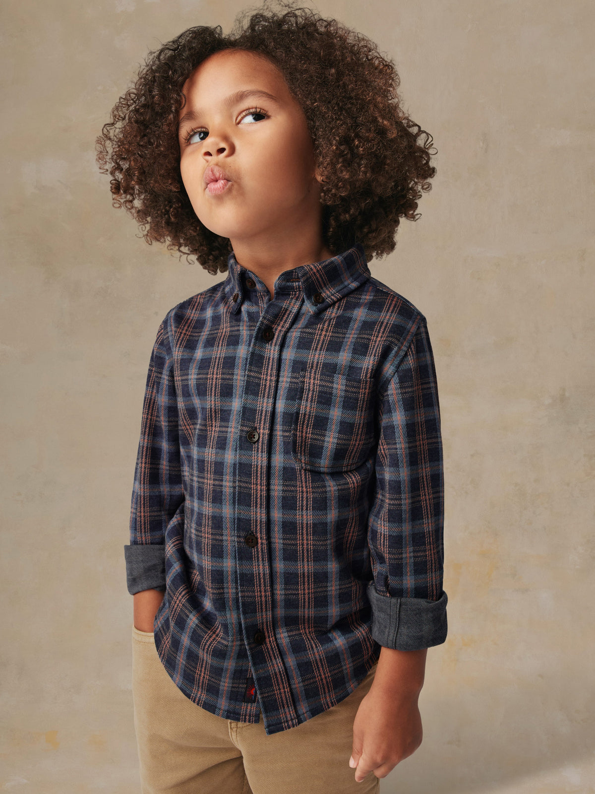 A child is wearing a plaid shirt and beige pants, image 2 of 6