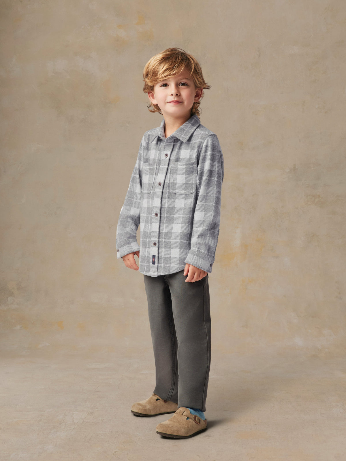 A child wearing a grey plaid button up shirt and grey pants, image 4 of 6