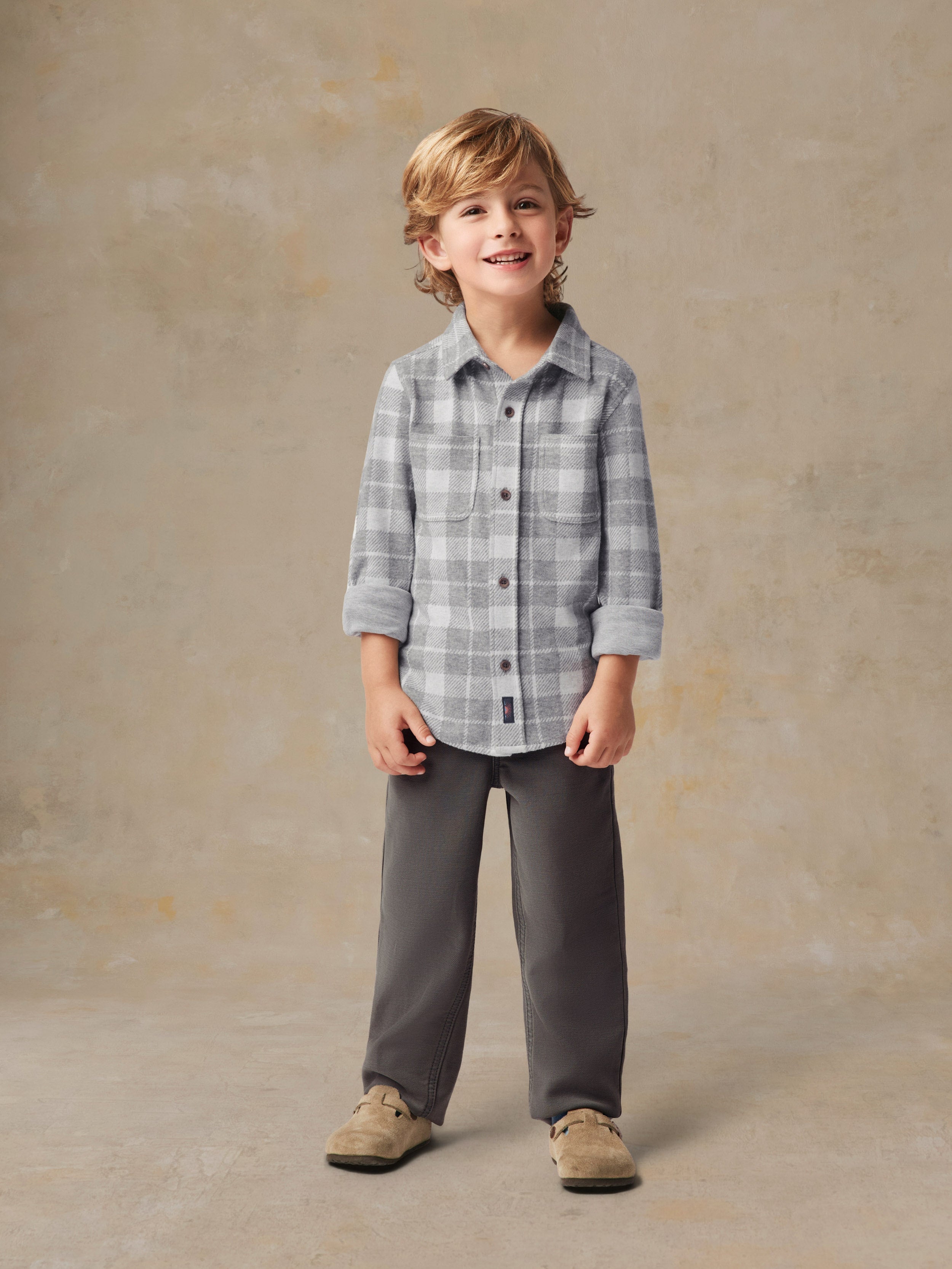 A child wearing a grey plaid button up shirt and grey pants