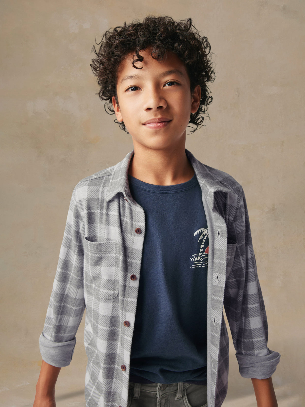 Close up of a child wearing a grey plaid button up shirt and grey pants, image 6 of 7