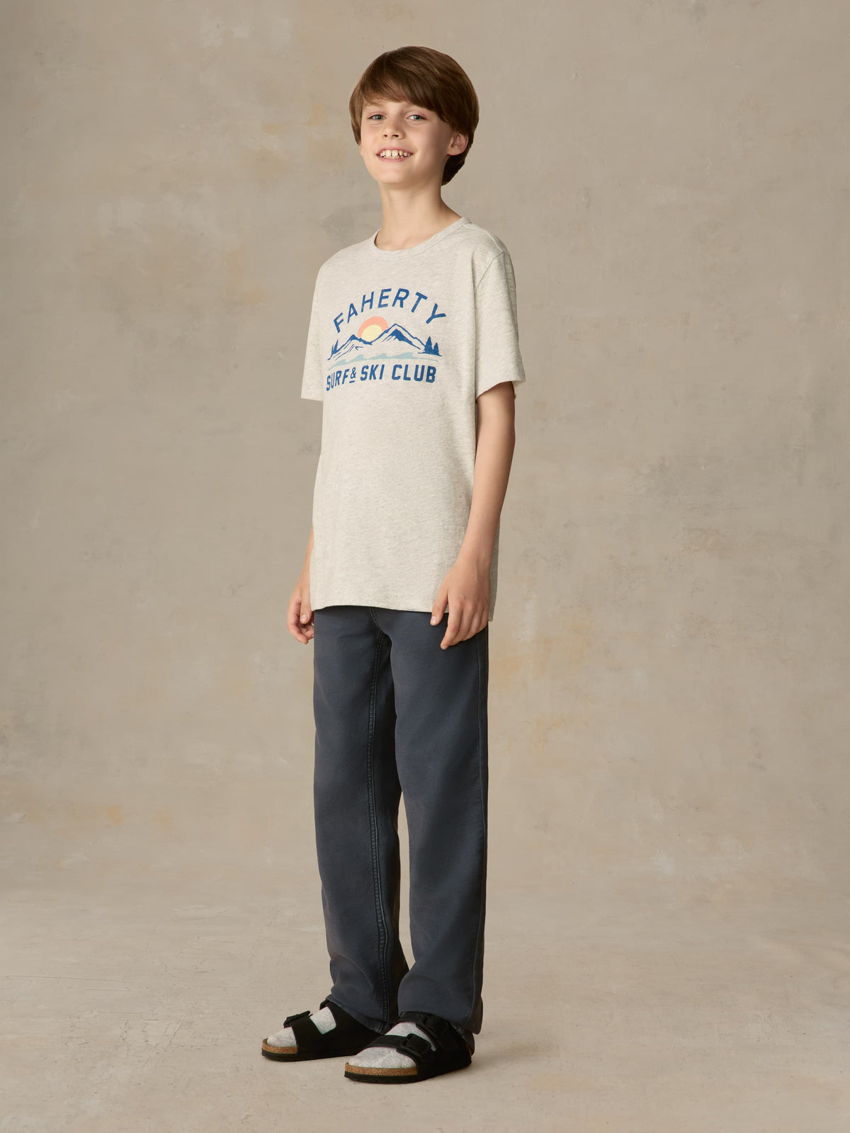 Child wearing a grey graphic tee with navy pants against a beige background, image 4 of 7