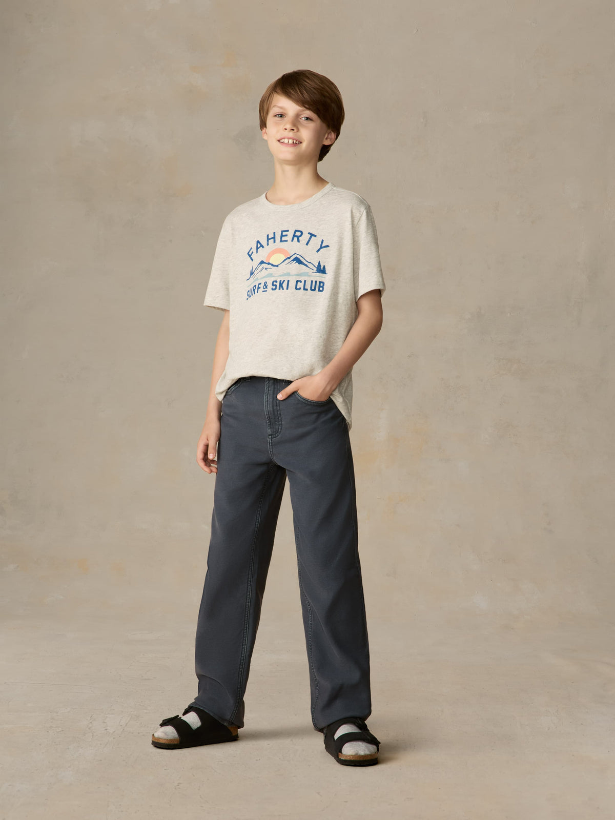 Child wearing a grey graphic tee with navy pants against a beige background, image 2 of 7