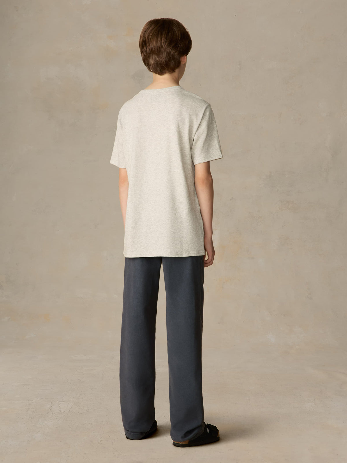 Child wearing a grey tee with navy pants against a beige background, image 3 of 7