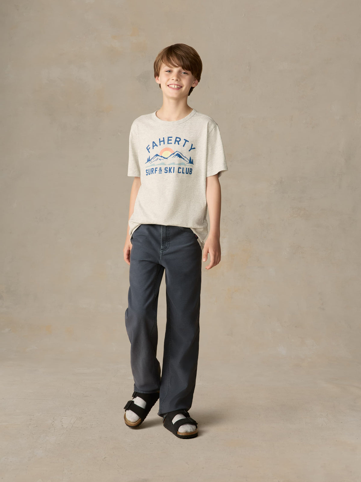 Child wearing a grey graphic tee with navy pants against a beige background, image 1 of 7
