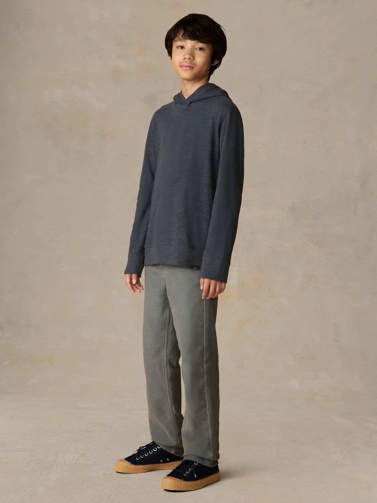 Child wearing a blue hoodie with grey pants against a beige background, image 2 of 6