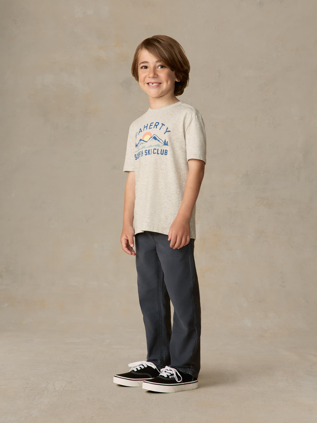 Child wearing graphic grey tee and navy pants against a beige background, image 2 of 6