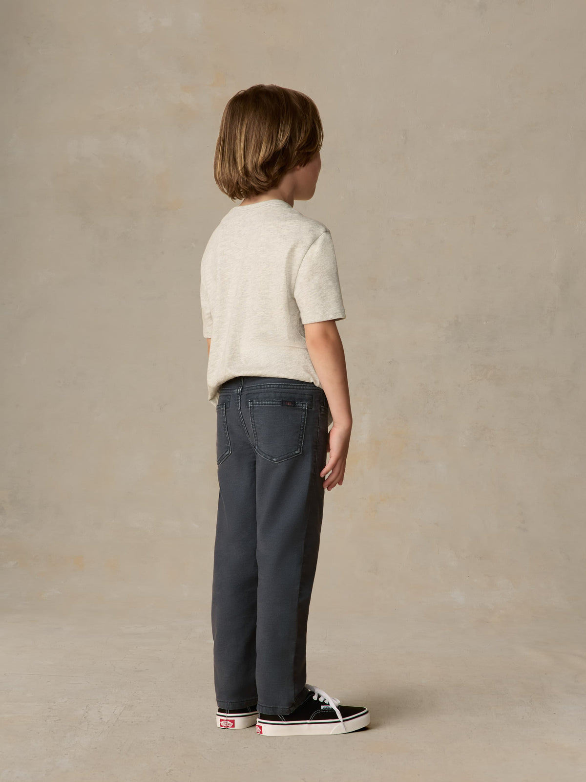 Child wearing graphic grey tee and navy pants against a beige background, image 3 of 6