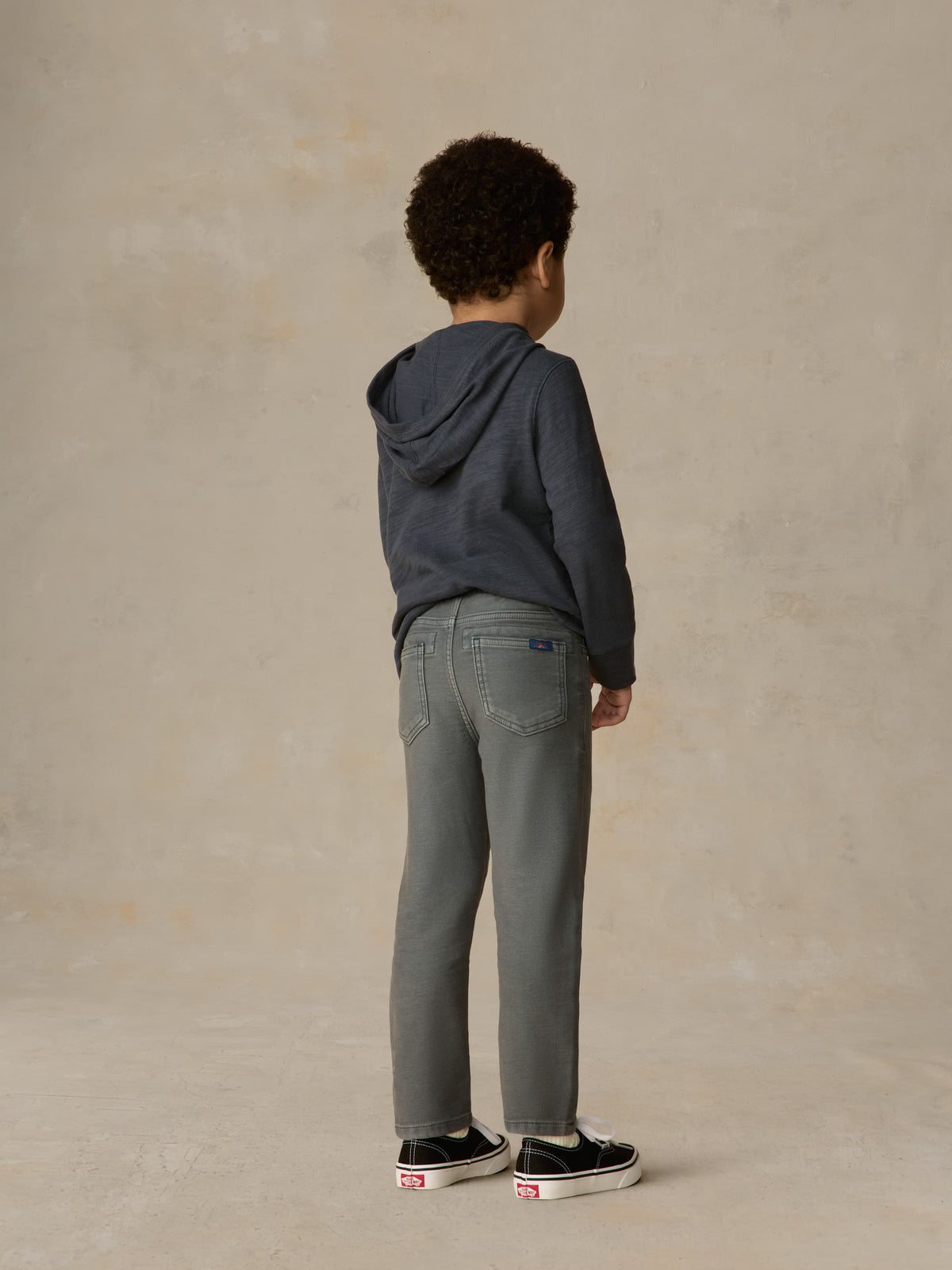 Child wearing blue hoodie and grey pants against a beige background, image 2 of 6