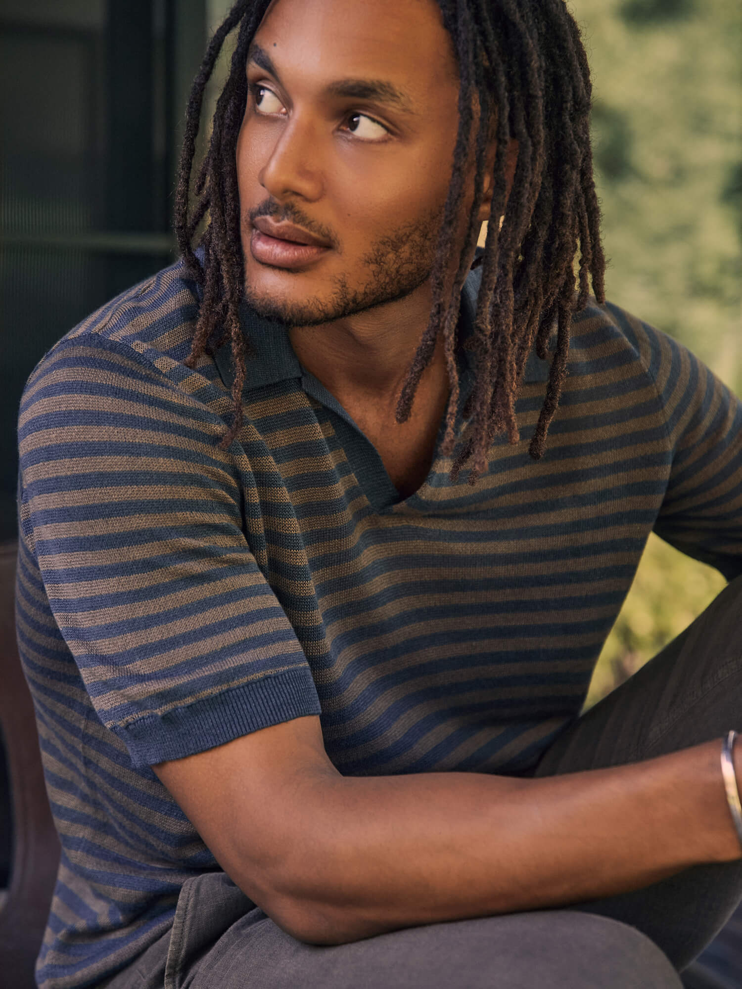 Man wearing a striped shirt sitting outdoors with a blurred background