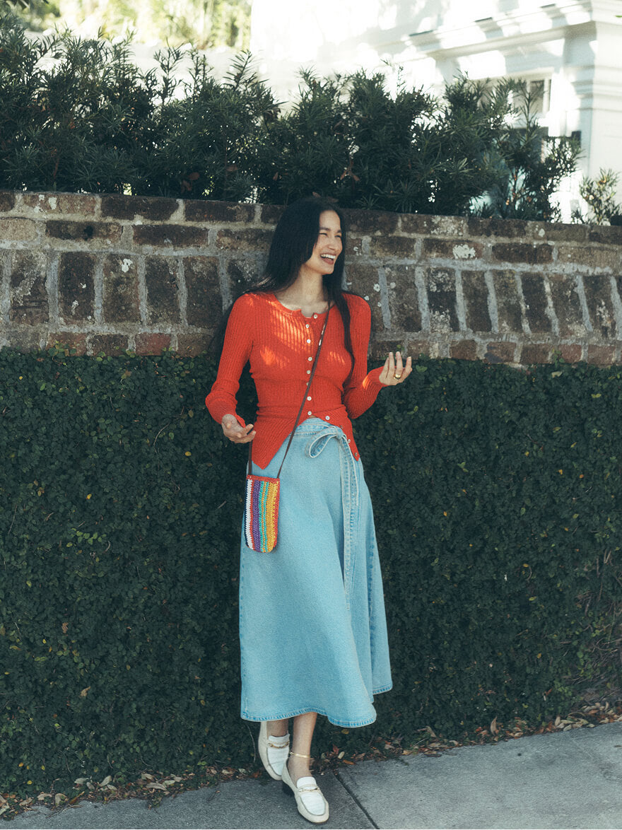 Woman standing in front of an ivy wall wearing a red pointelle cardigan paired with a light blue denim skirt
