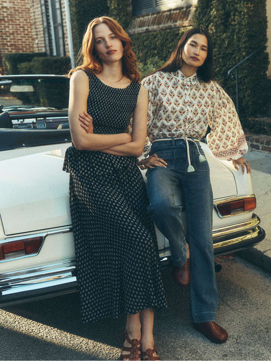Two women sitting on a vintage mercedes benz, one wearing a matching set of a smocked top and a skirt, the other wearing a floral blouse and stretch terry pants