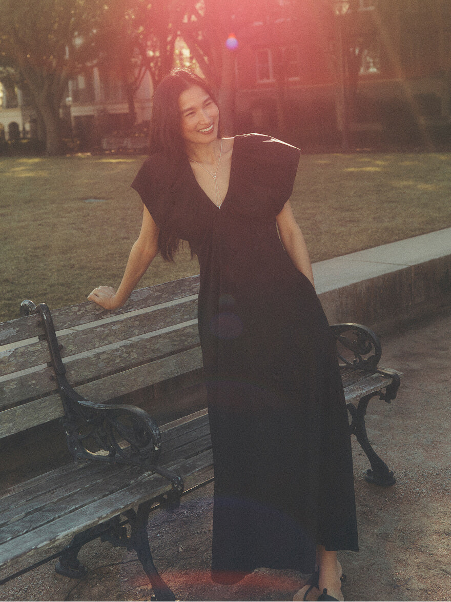 A woman in a black dress standing next to a park bench with