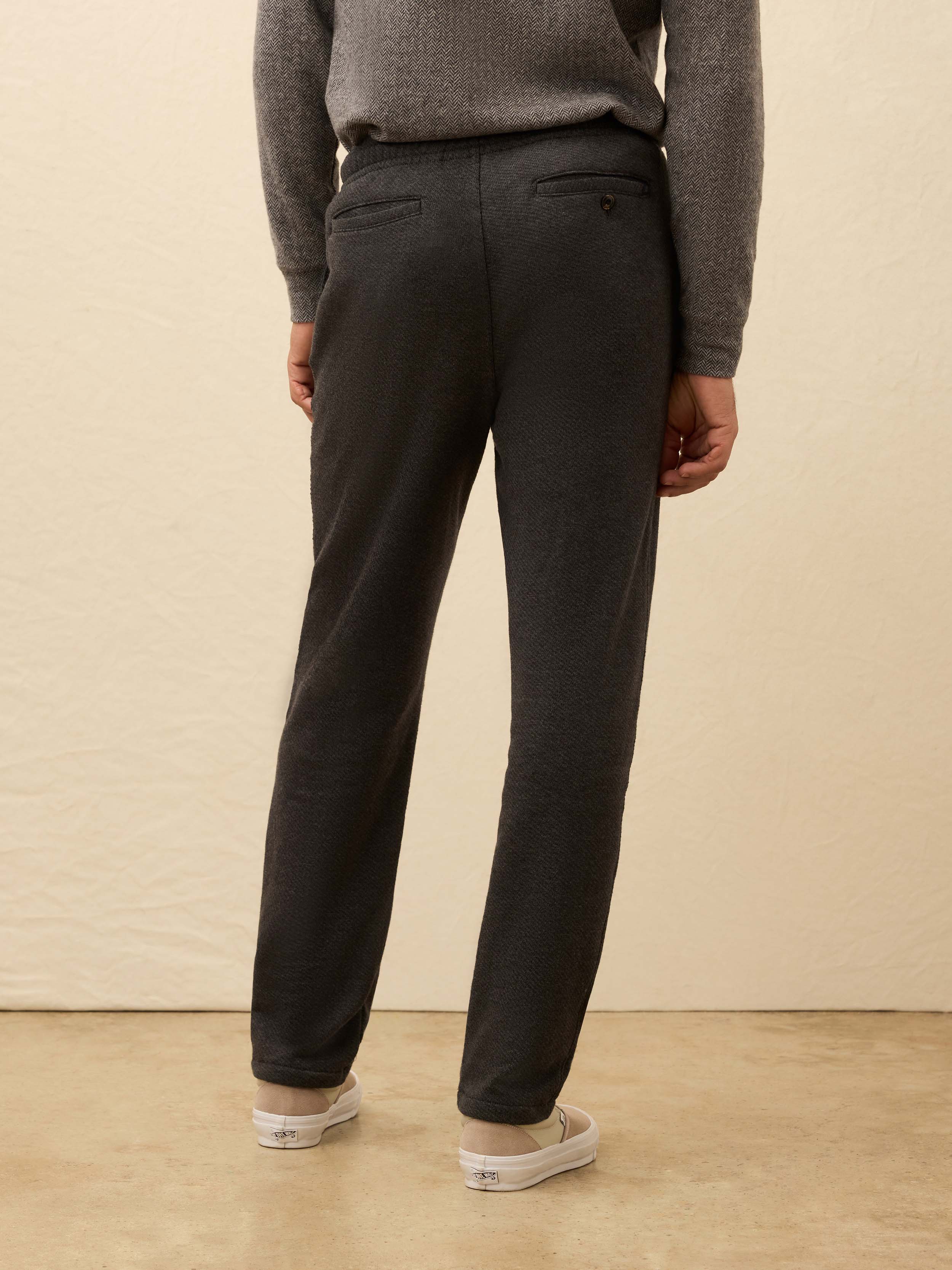 Man wearing a light gray sweater and dark grey jogger pants against a beige background