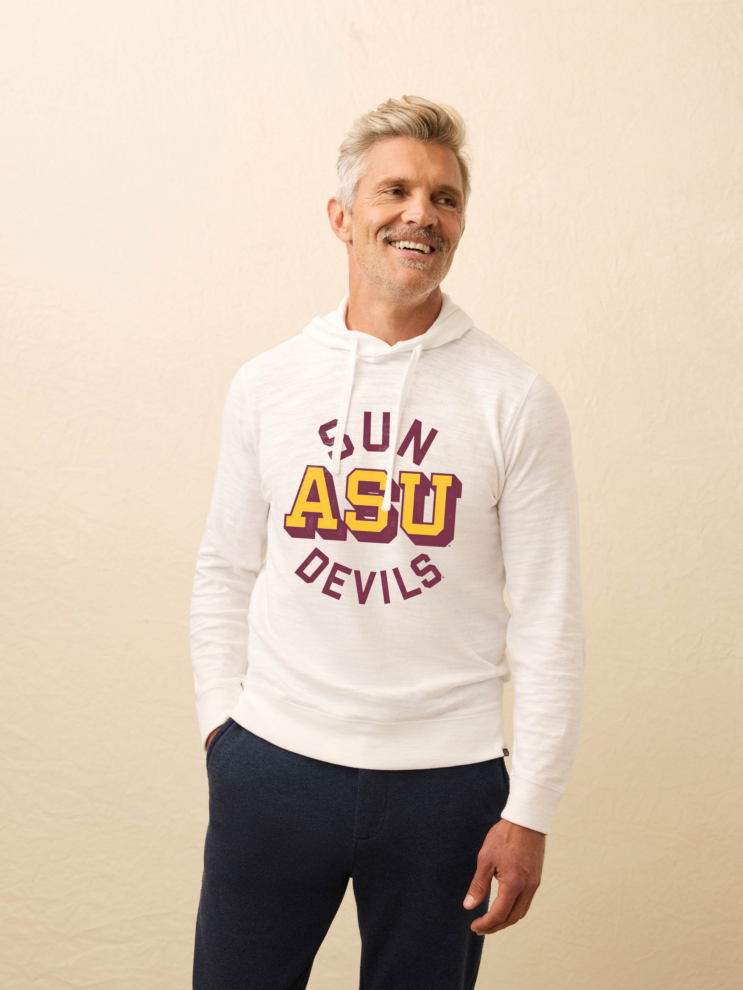 Man wearing a white hoodie with ASU graphic at the center front against a beige background
