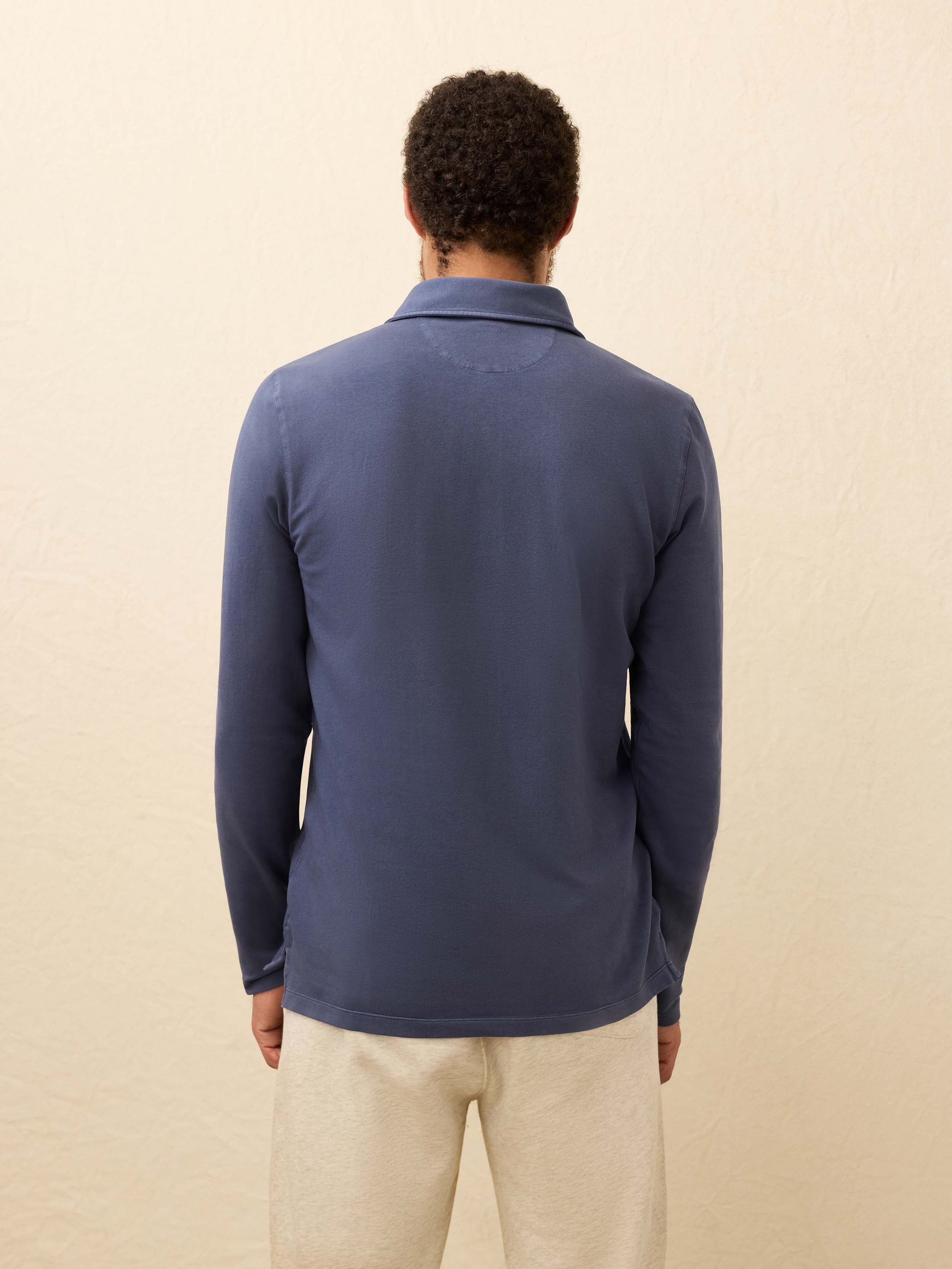 Man wearing a blue long-sleeve polo shirt against a beige background