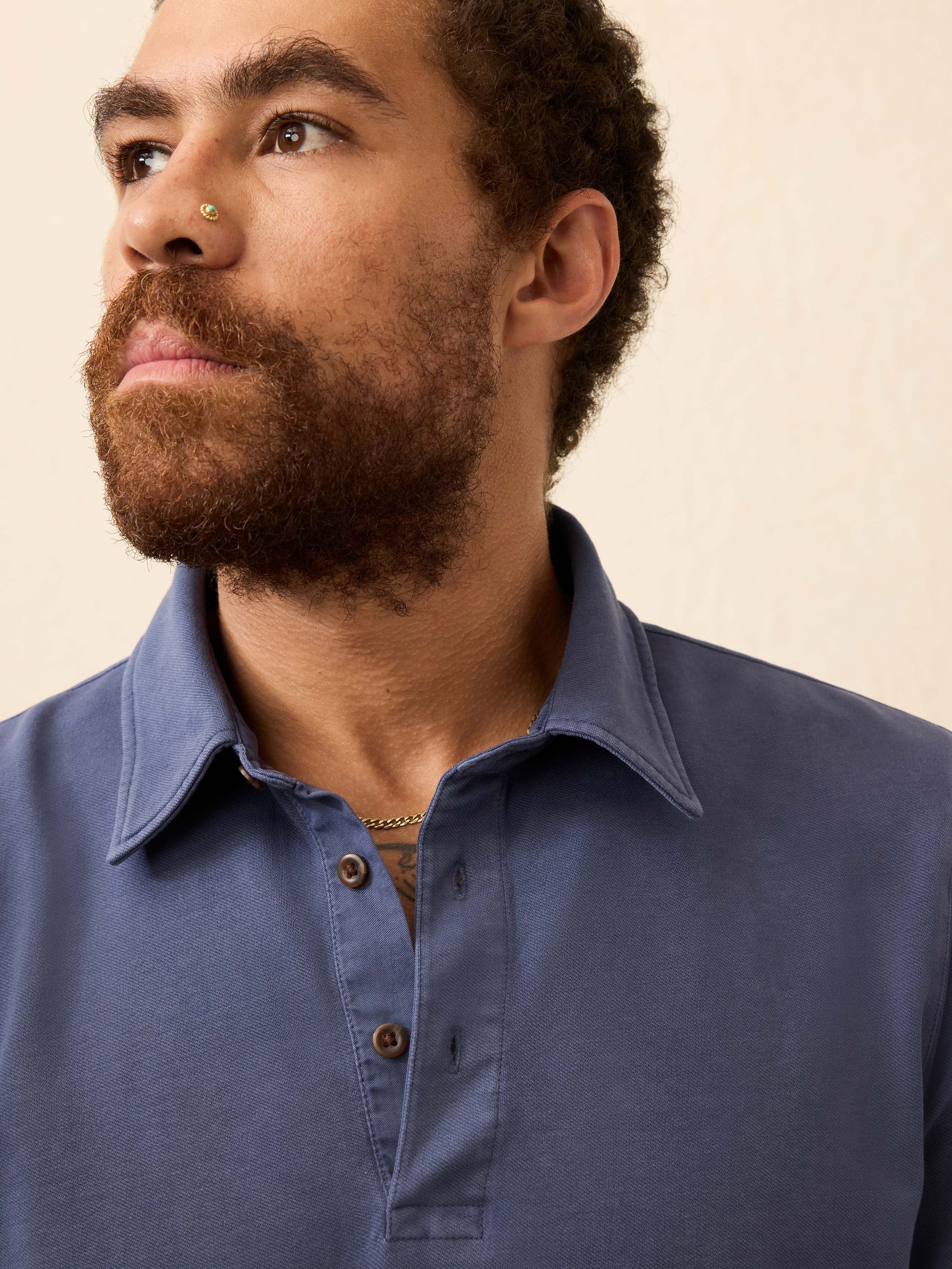 Man wearing a blue long-sleeve polo shirt against a beige background