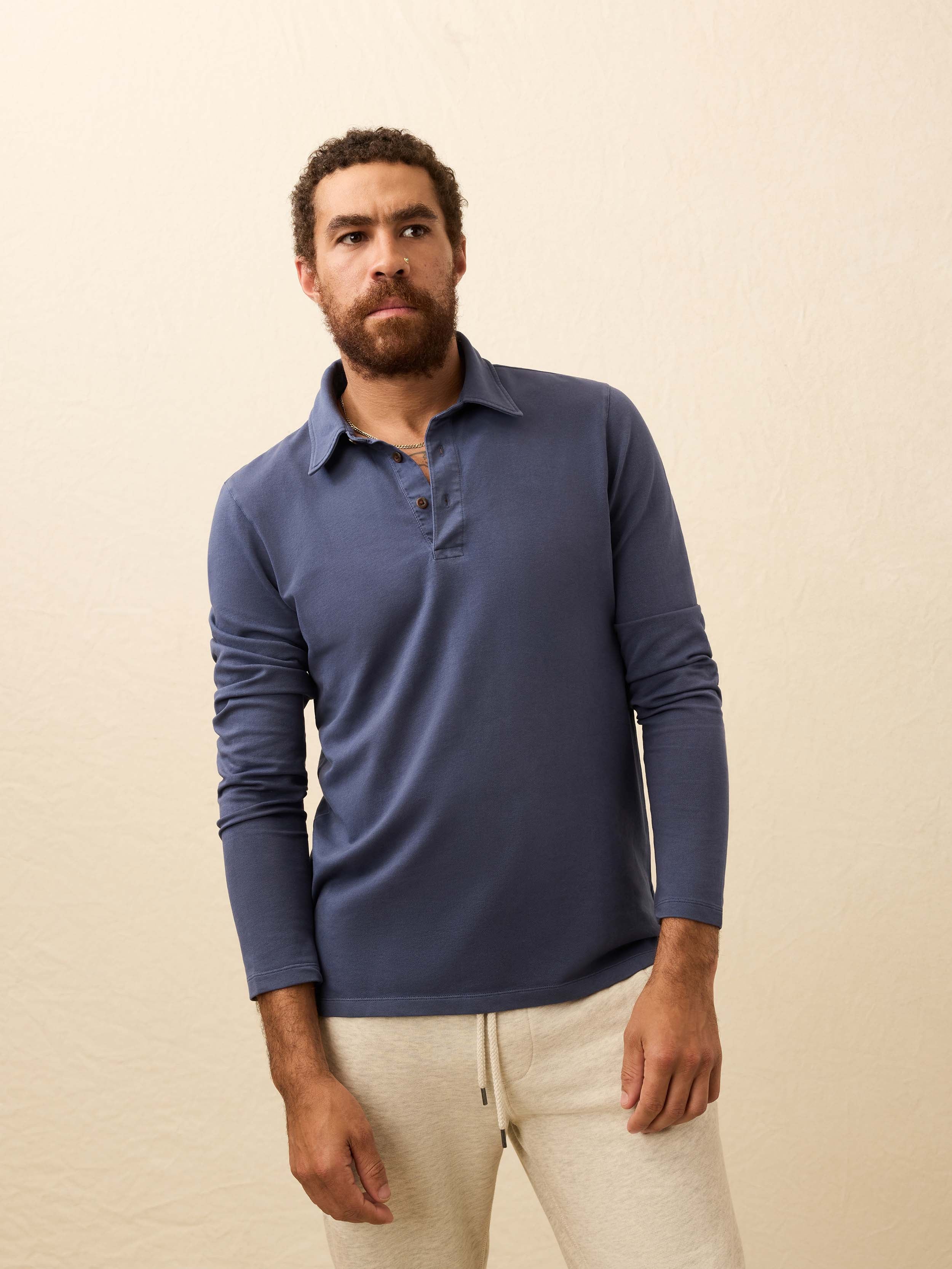 Man wearing a blue long-sleeve polo shirt against a beige background