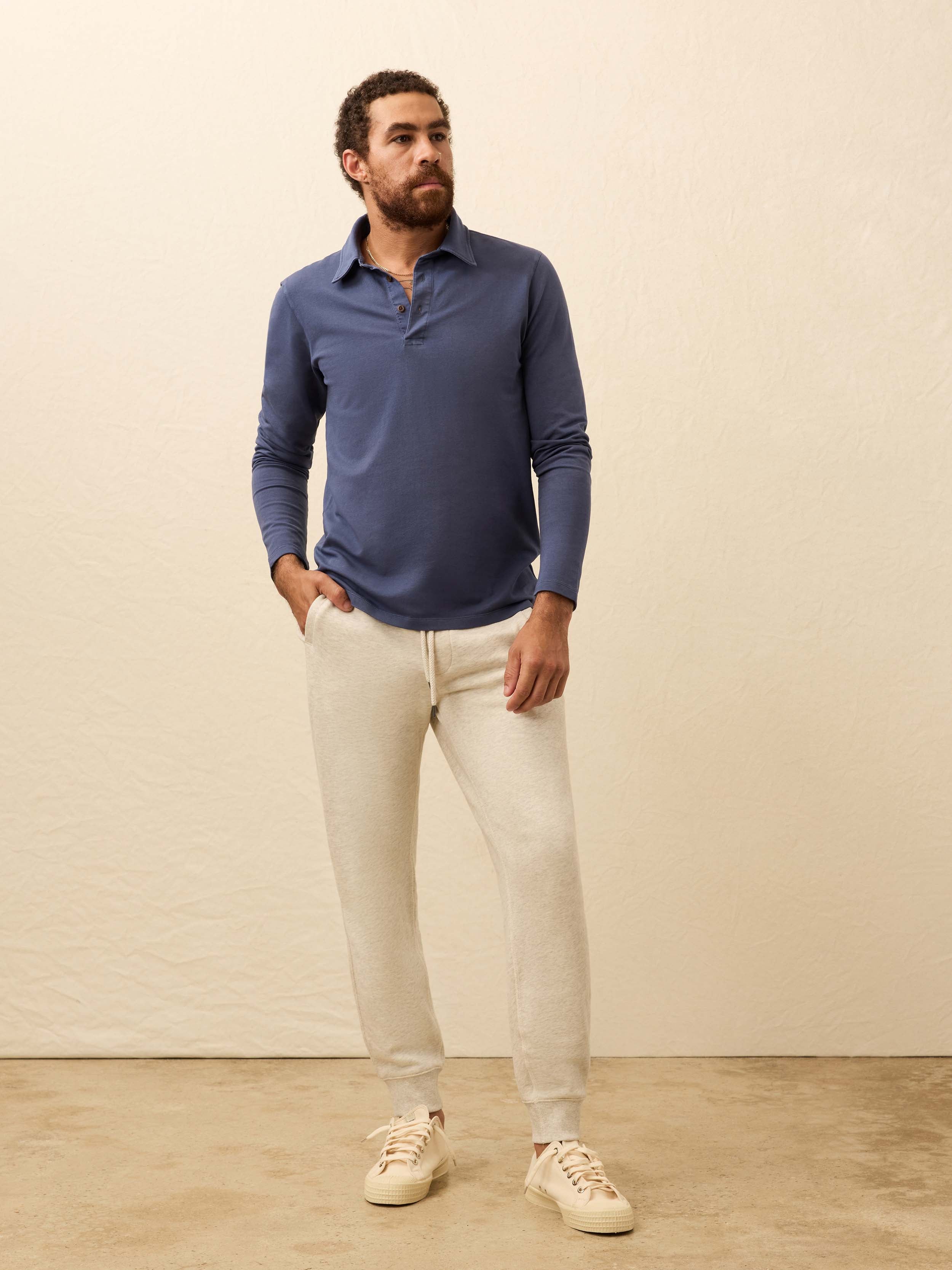 Man wearing a blue long-sleeve polo shirt against a beige background