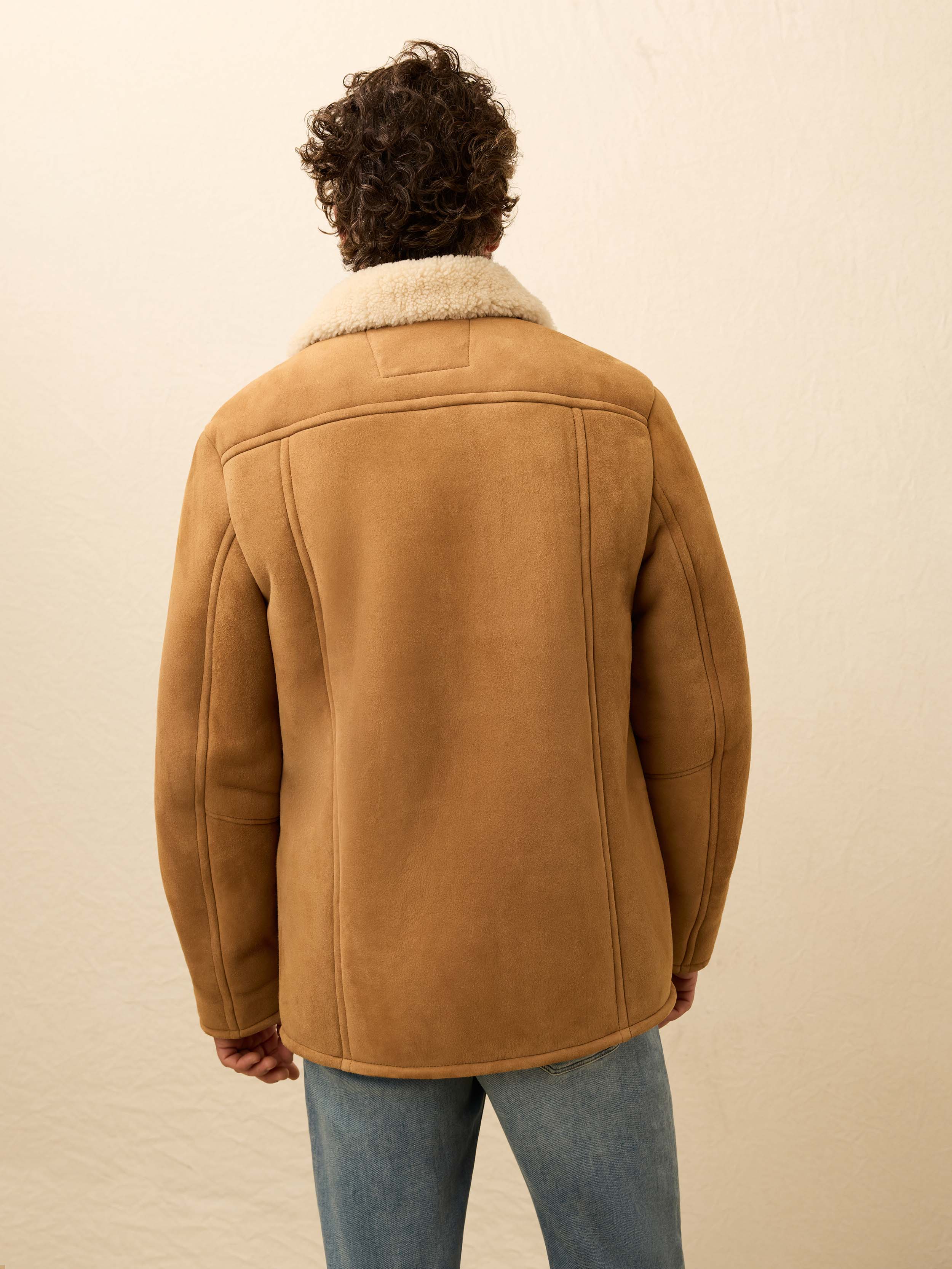 Man wearing a brown suede shearling jacket against a beige wall