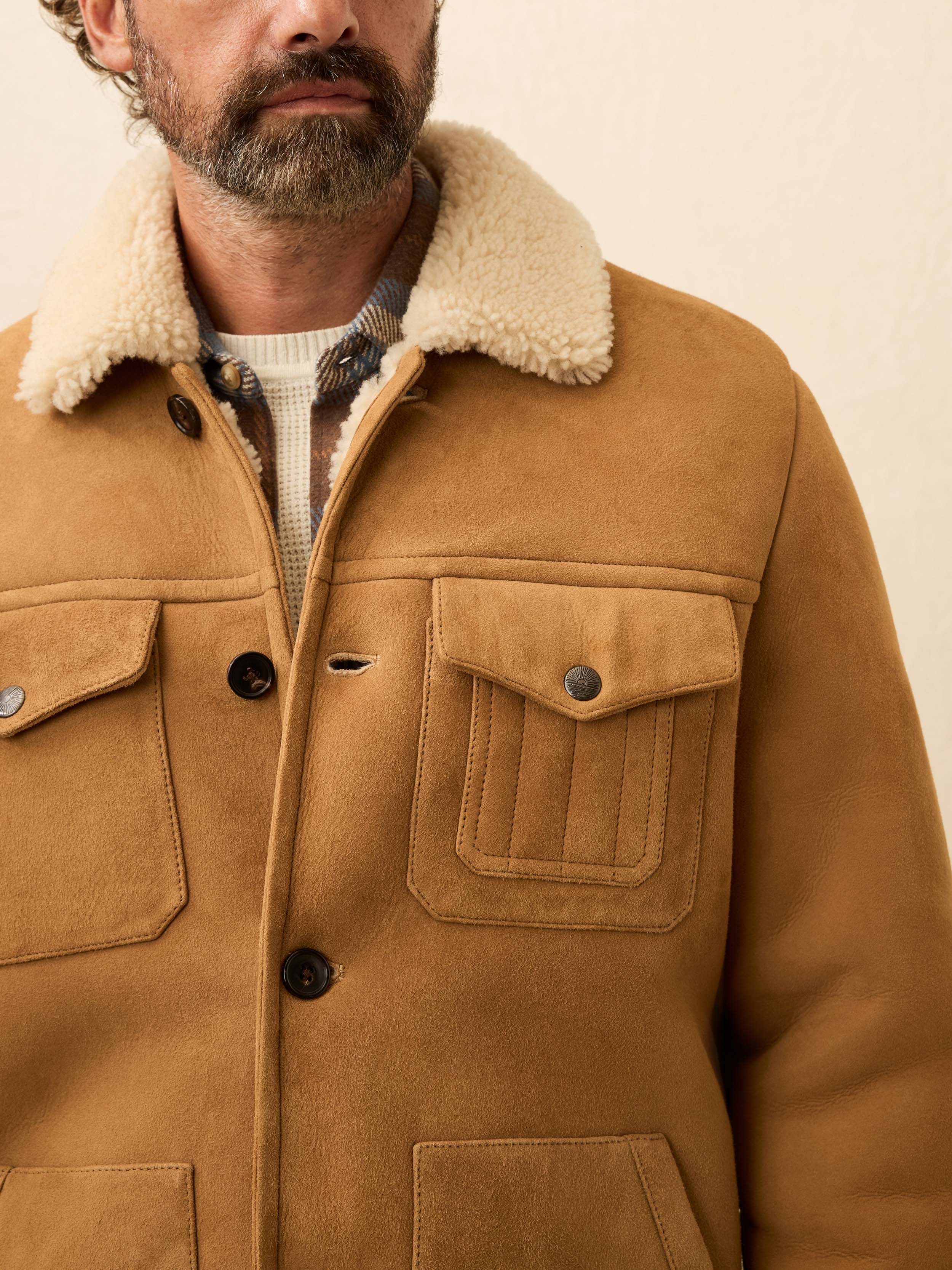 Brown suede shearling jacket with shearling collar worn by a man on a beige background
