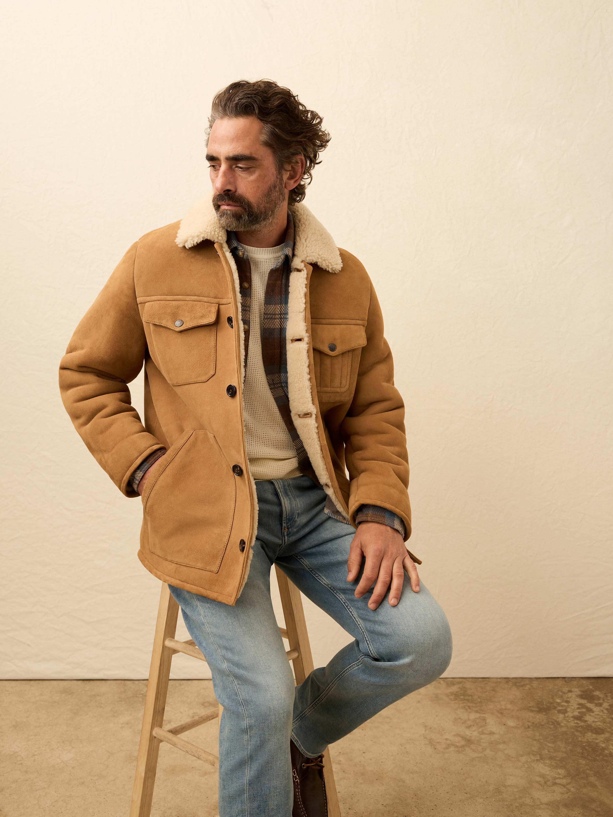 Man wearing a brown suede shearling jacket against a beige wall