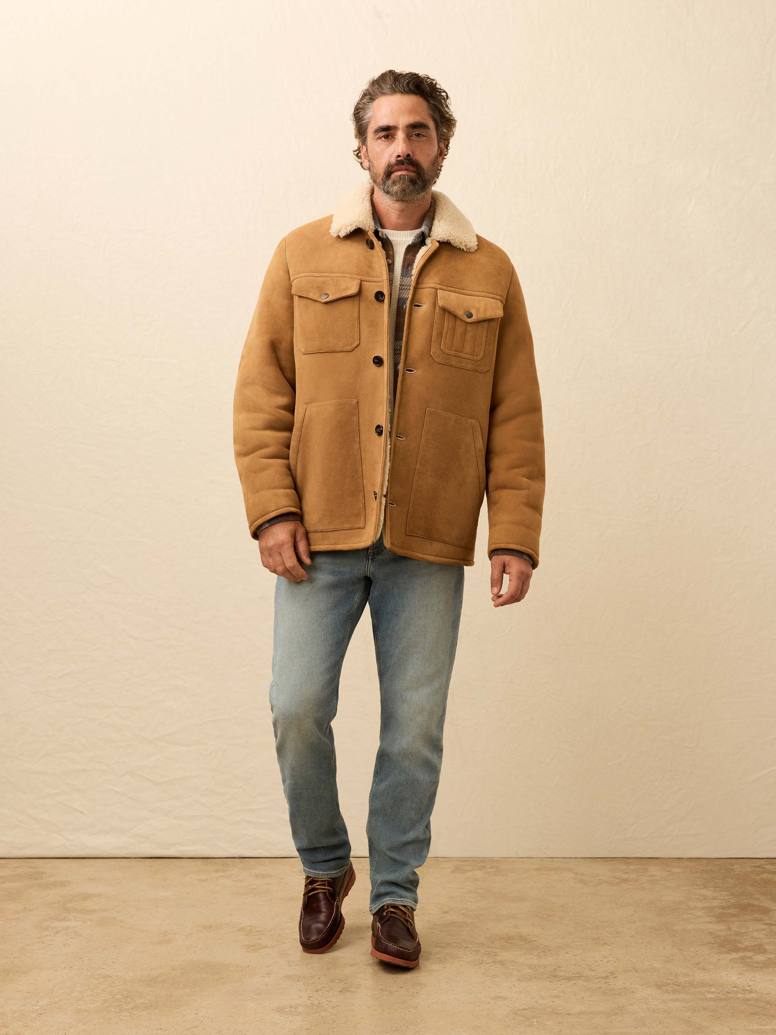Man wearing a brown suede shearling jacket against a beige wall