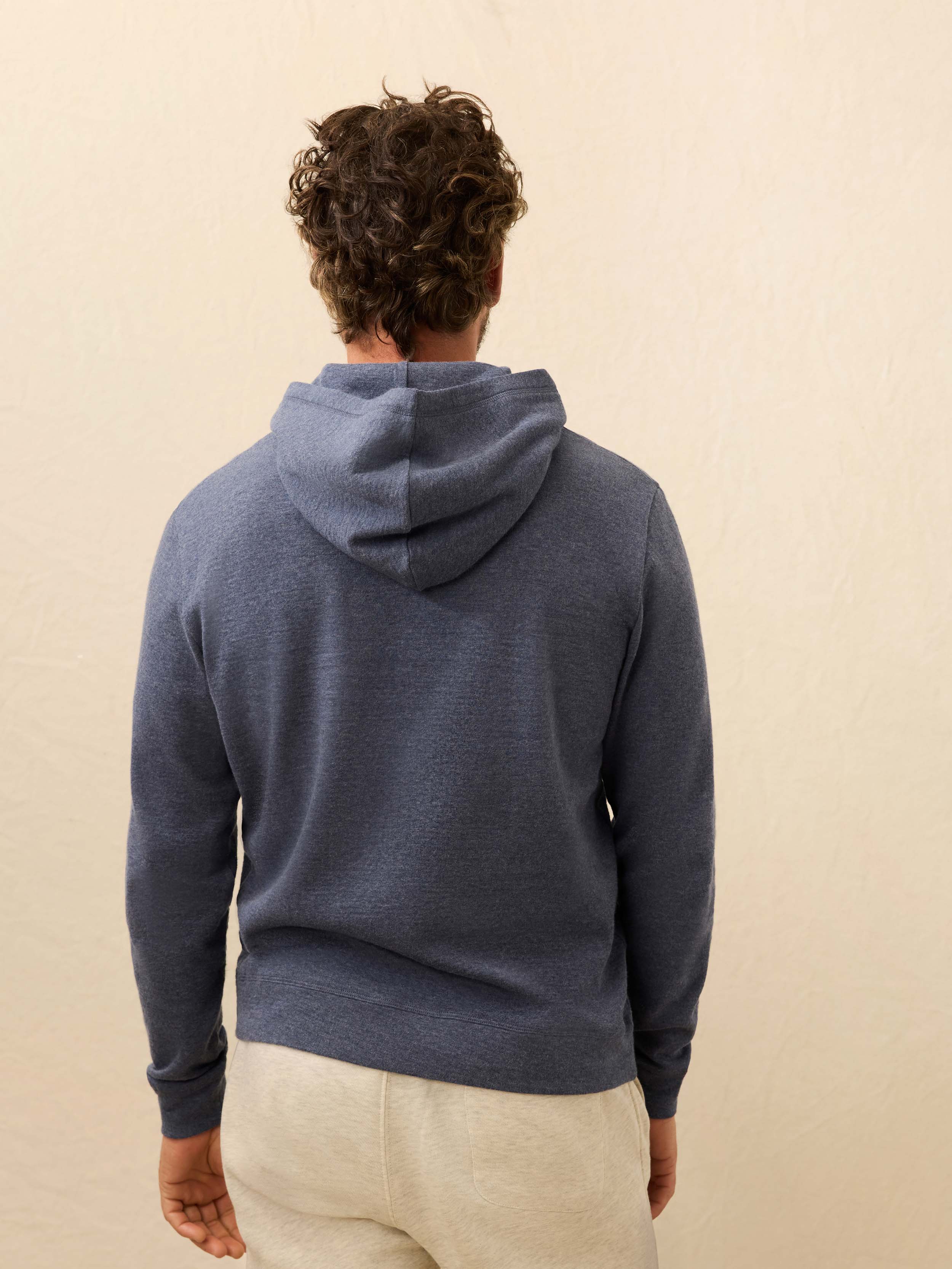 Man wearing a blue cashmere hoodie with sweatpants against a beige background
